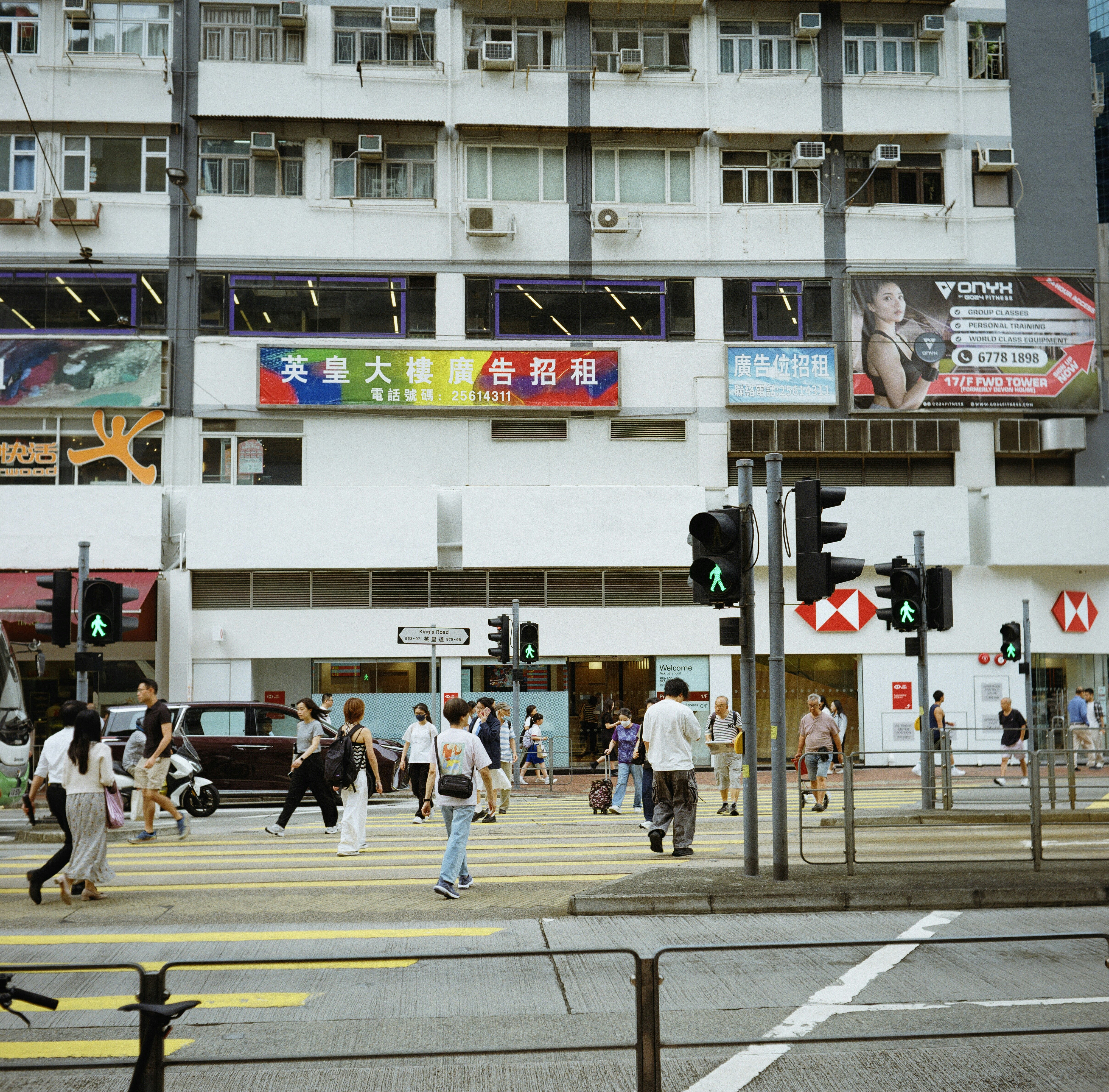 Pedestrians crossing a busy street in front of urban buildings.