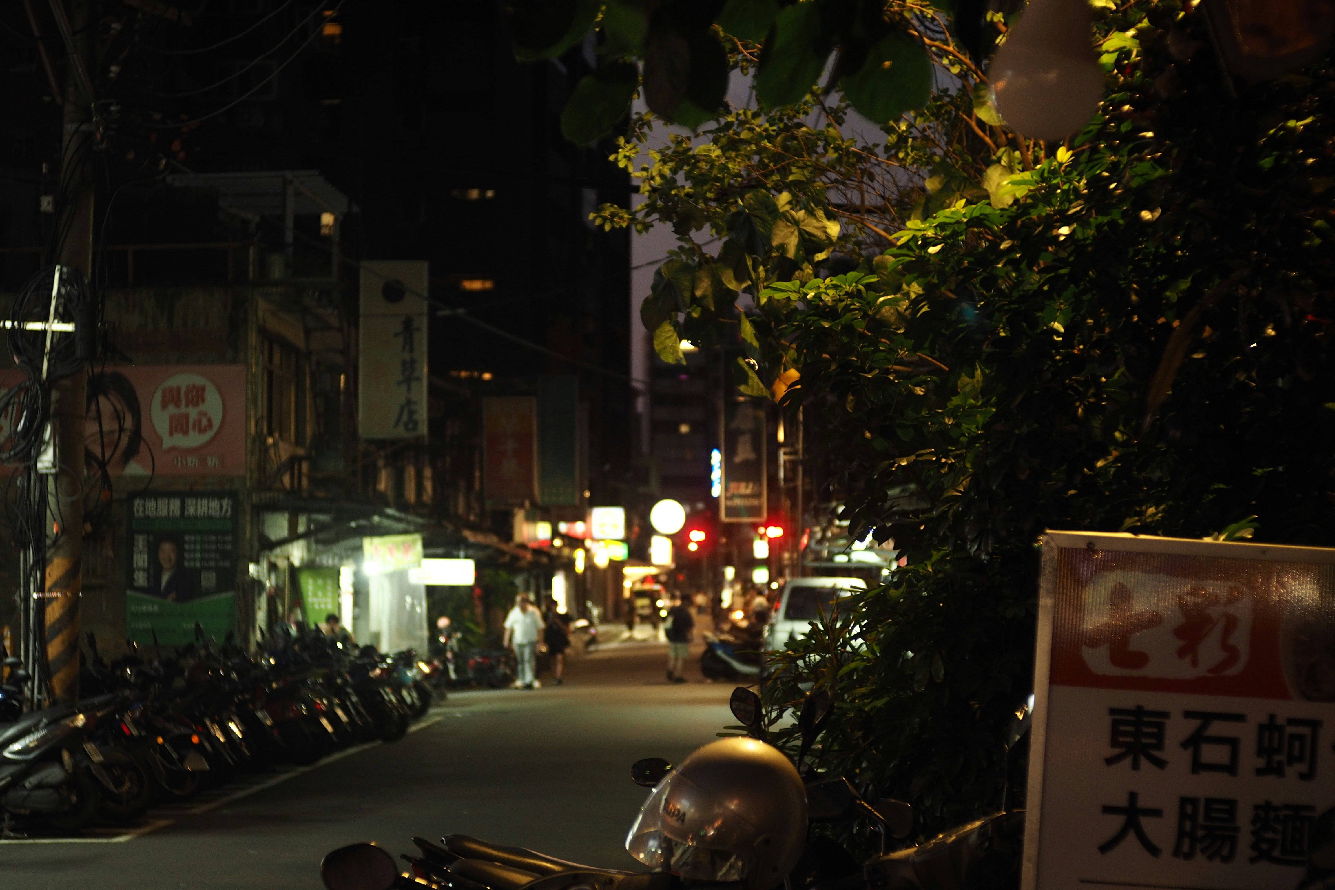 建物や駐車されたバイク、光る店の看板が並ぶ夜の通り。