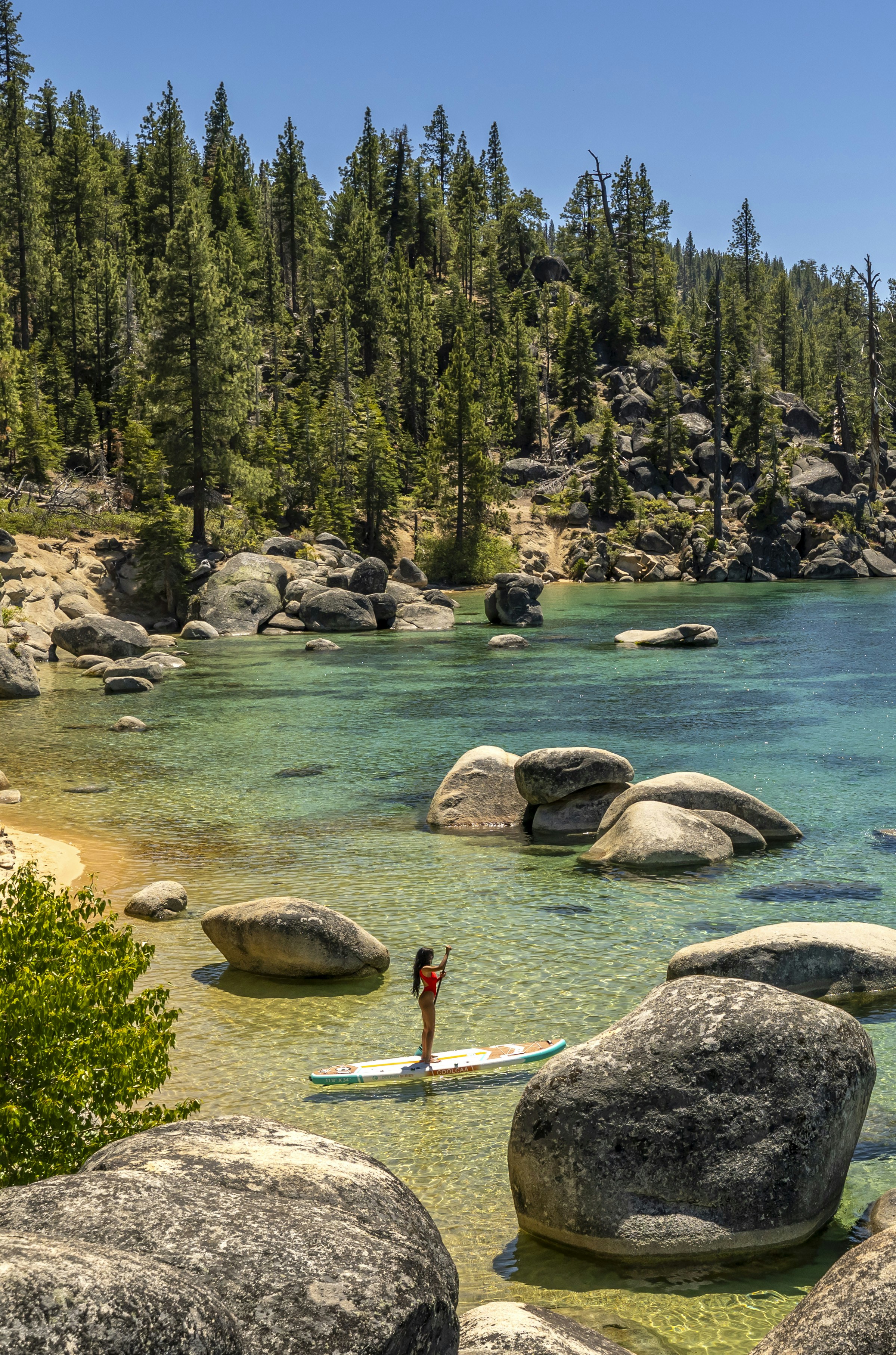 Woman paddleboarding on clear lake water with rocks and trees.