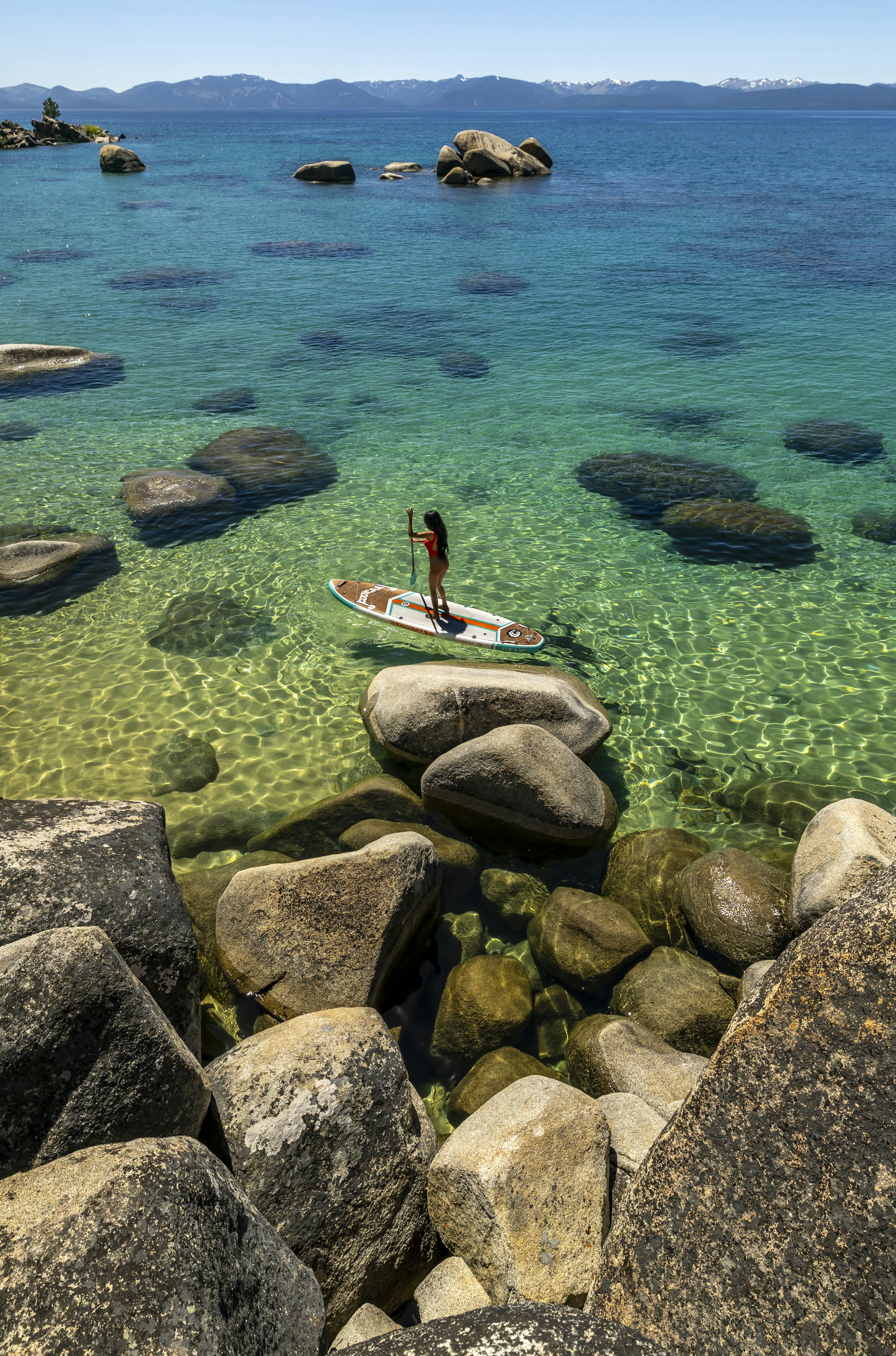 Paddleboarder on crystal clear lake water surrounded by rocks.