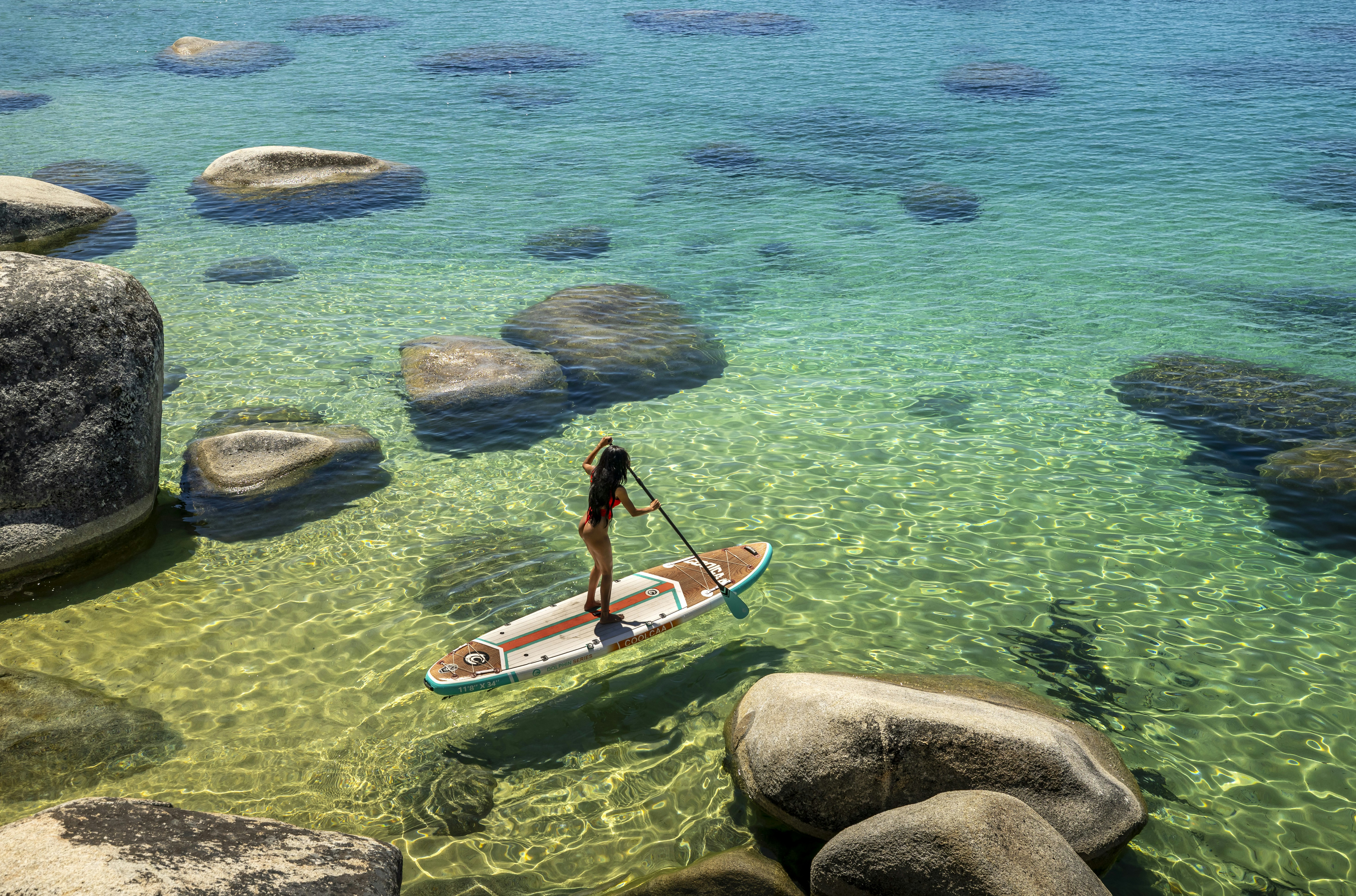 A person paddleboarding on clear turquoise water with submerged rocks
