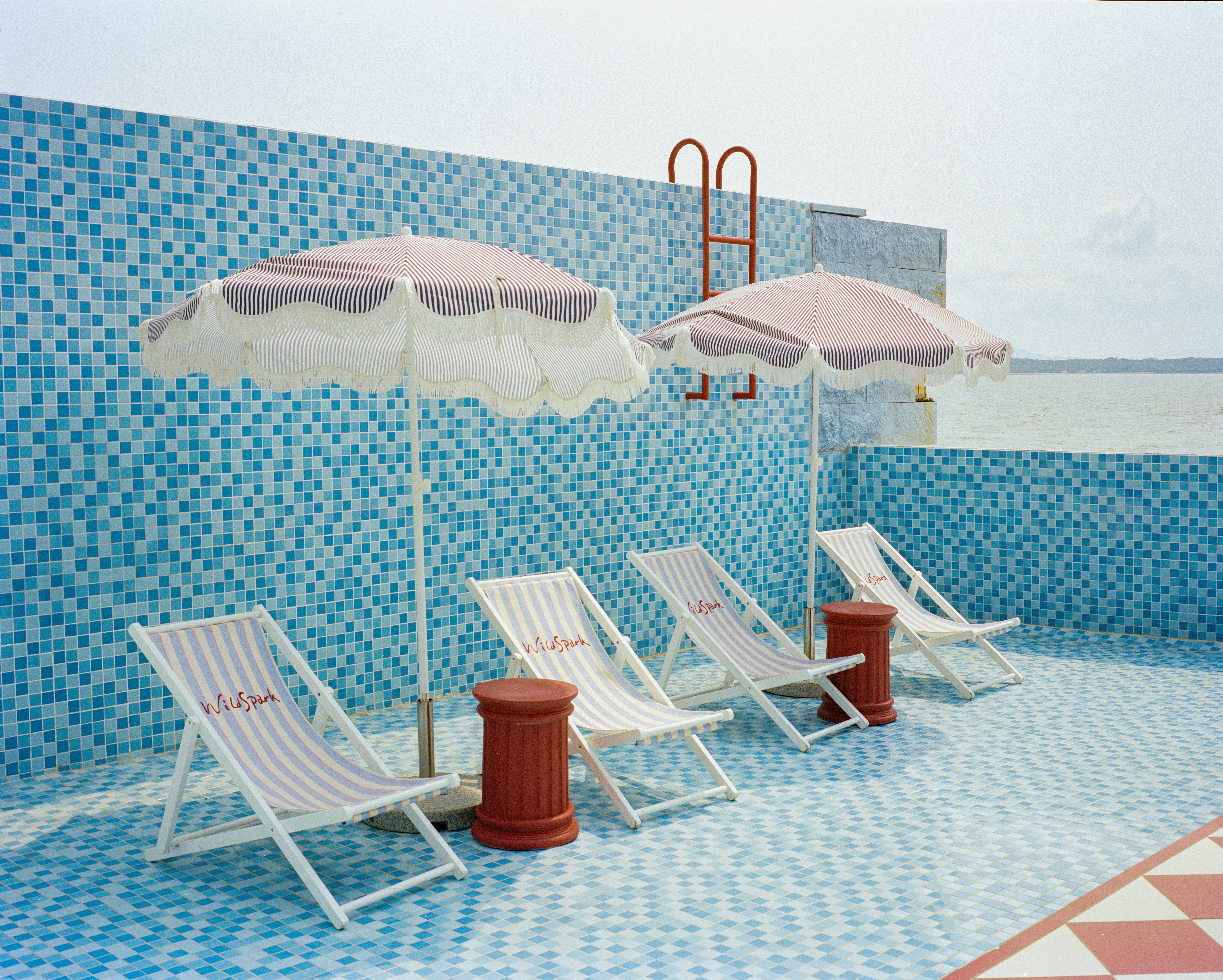 Blue tiled pool area with lounge chairs and pink umbrellas.