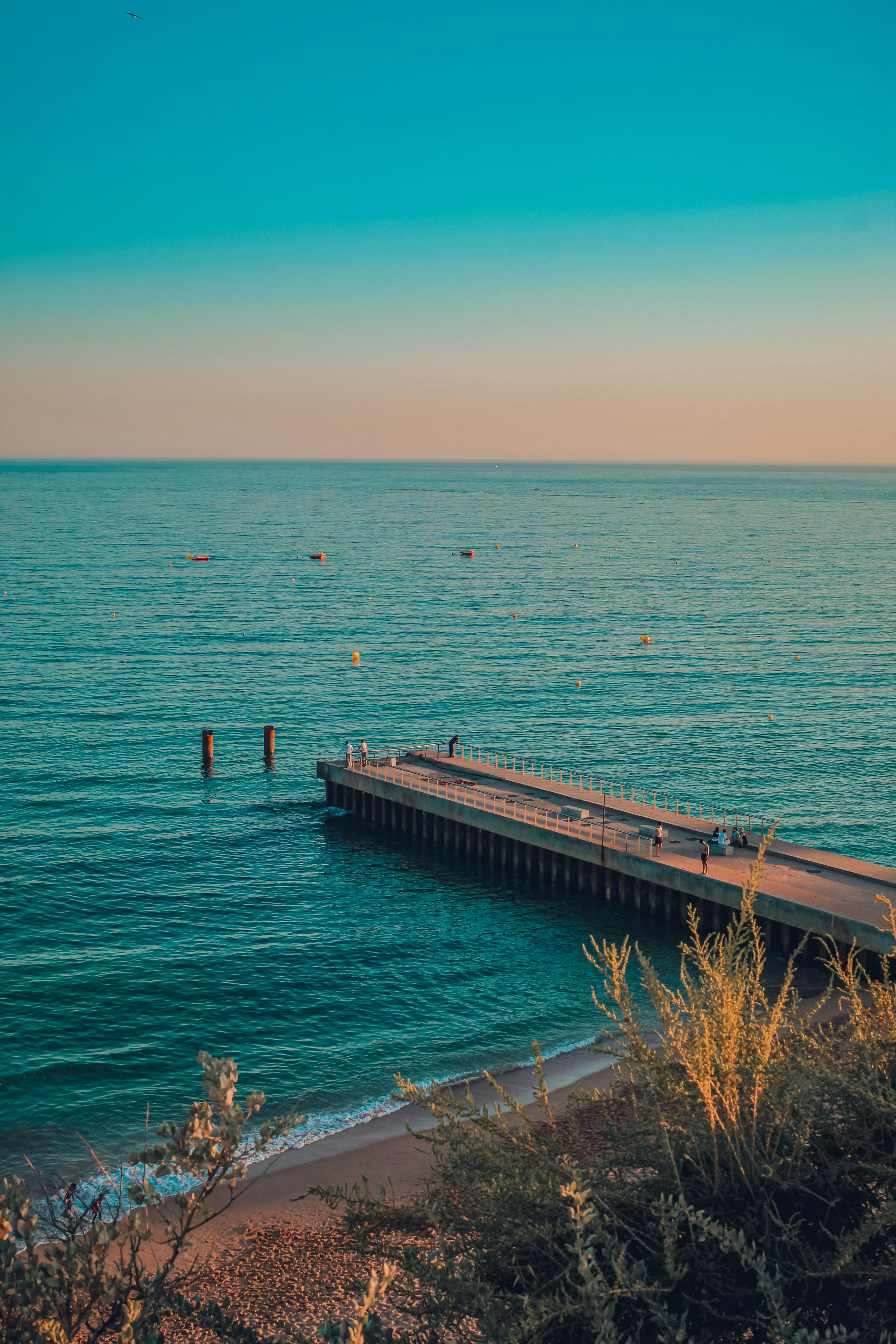 A long pier extends into the calm ocean at sunset
