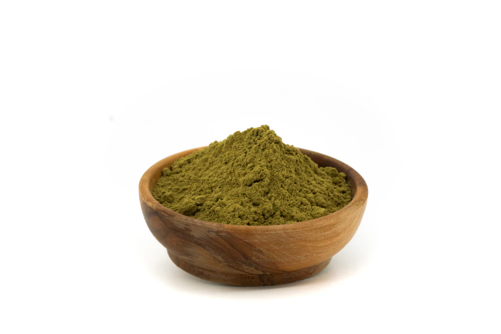 Green moringa leaf powder in a wooden bowl