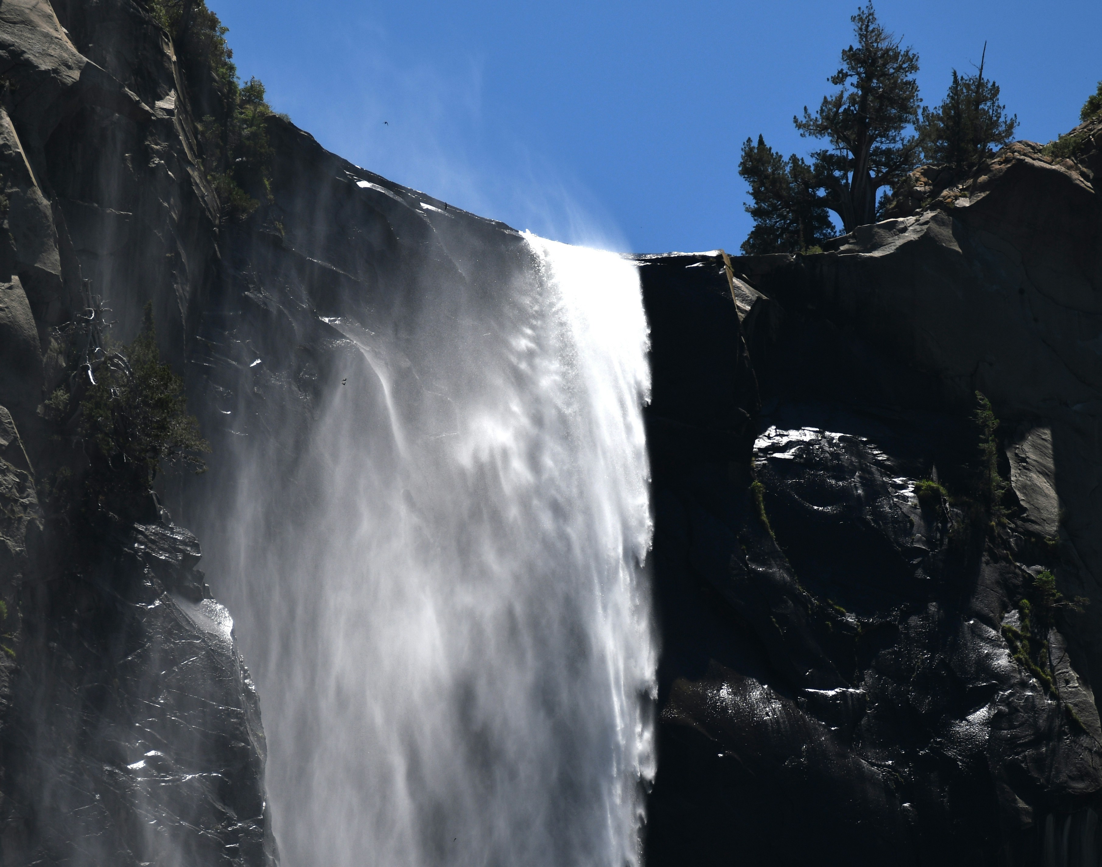 Une majestueuse cascade dévale une falaise sombre sous un ciel bleu clair.