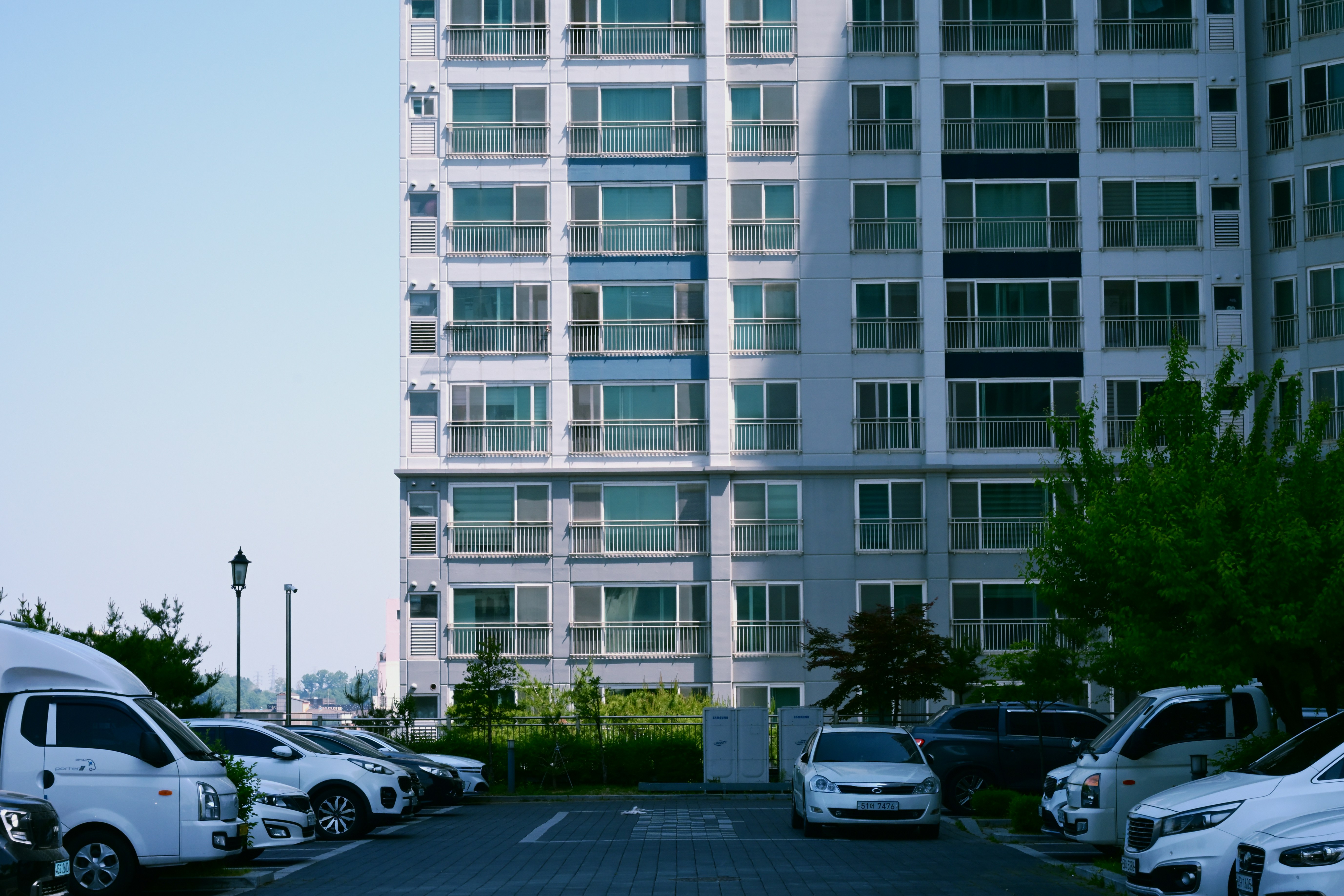 An apartment building overlooks a parking lot filled with cars.