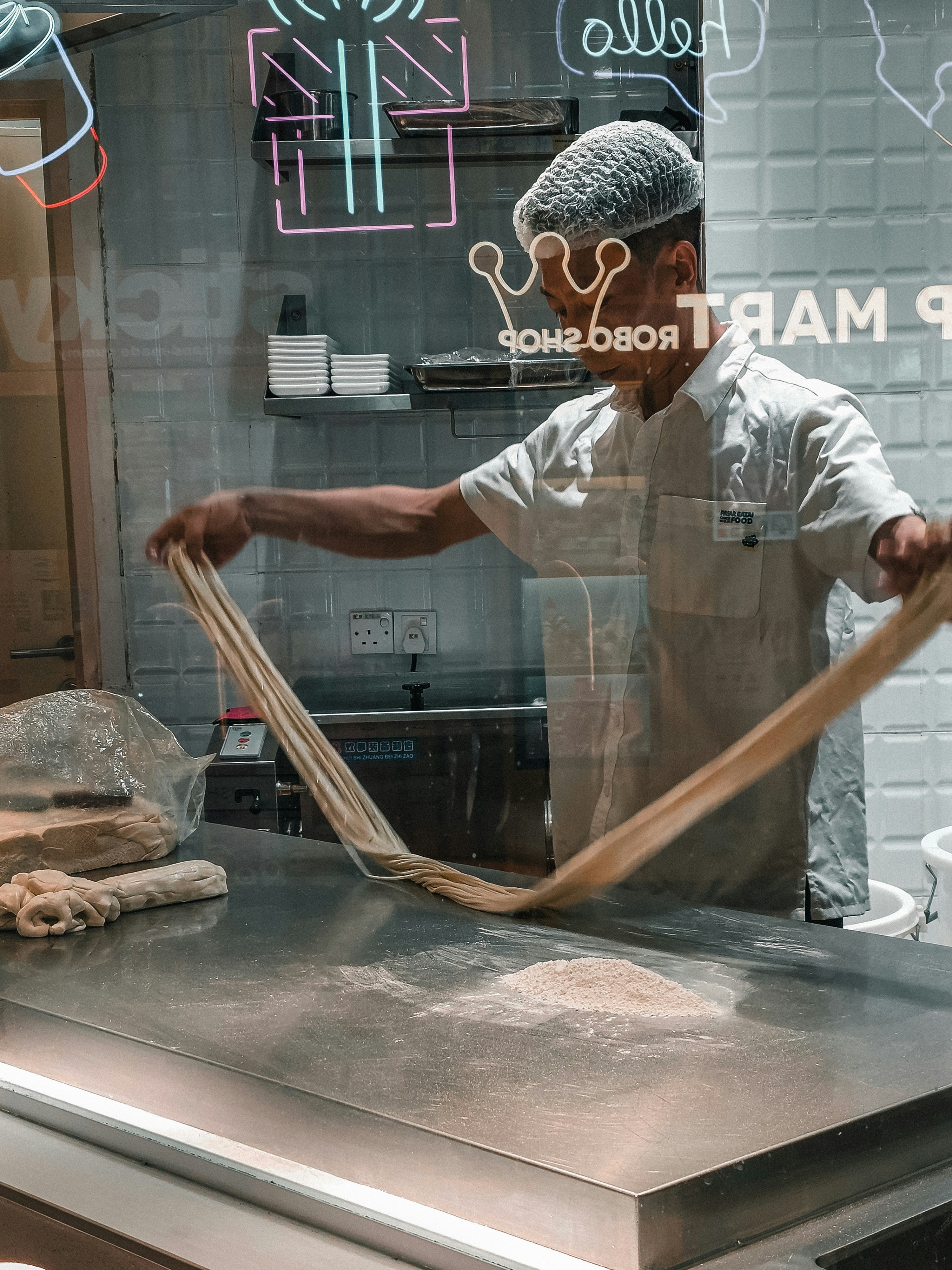Man stretching dough on a metal counter in a kitchen.