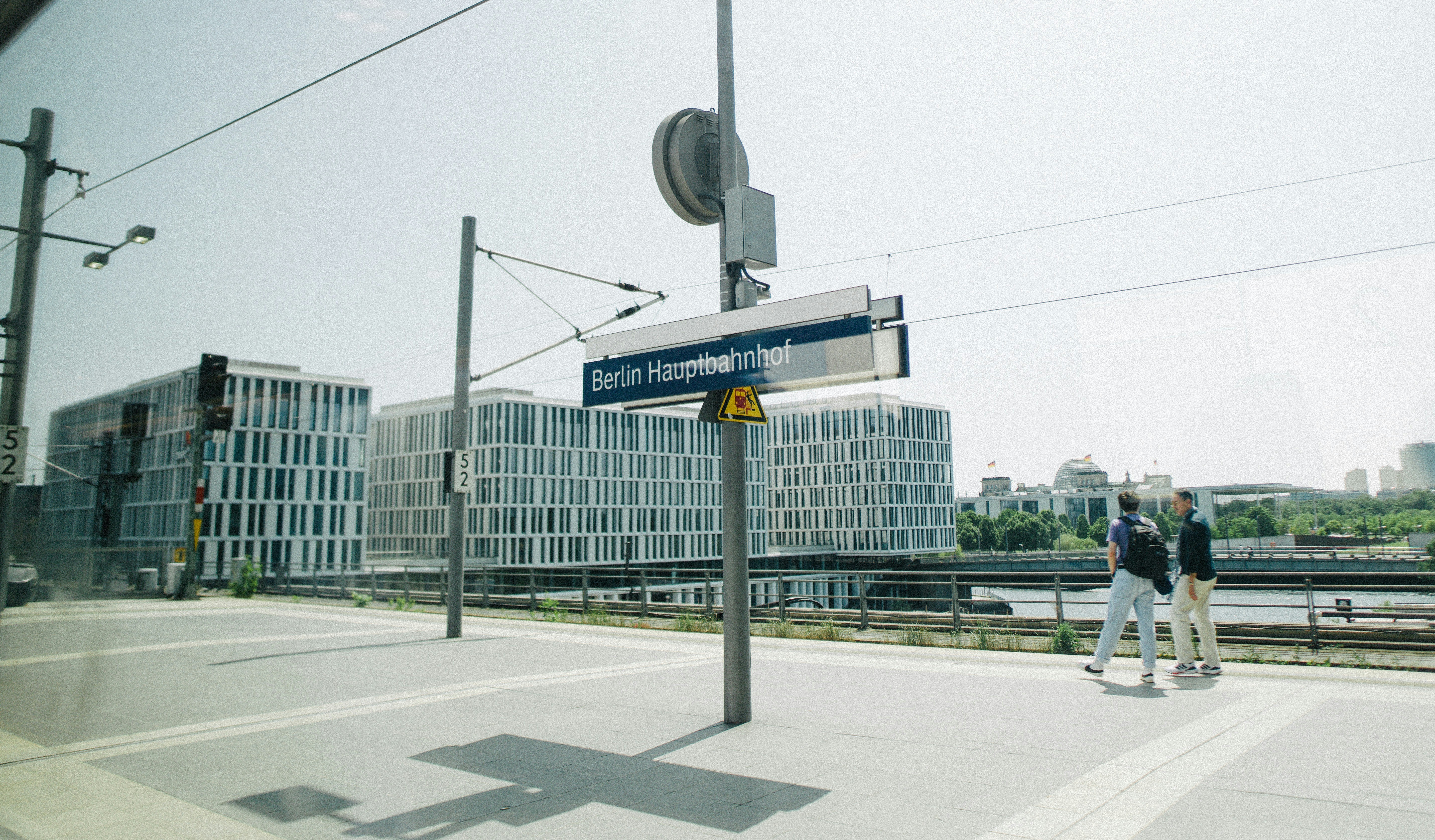 People walk on a train platform with modern buildings.