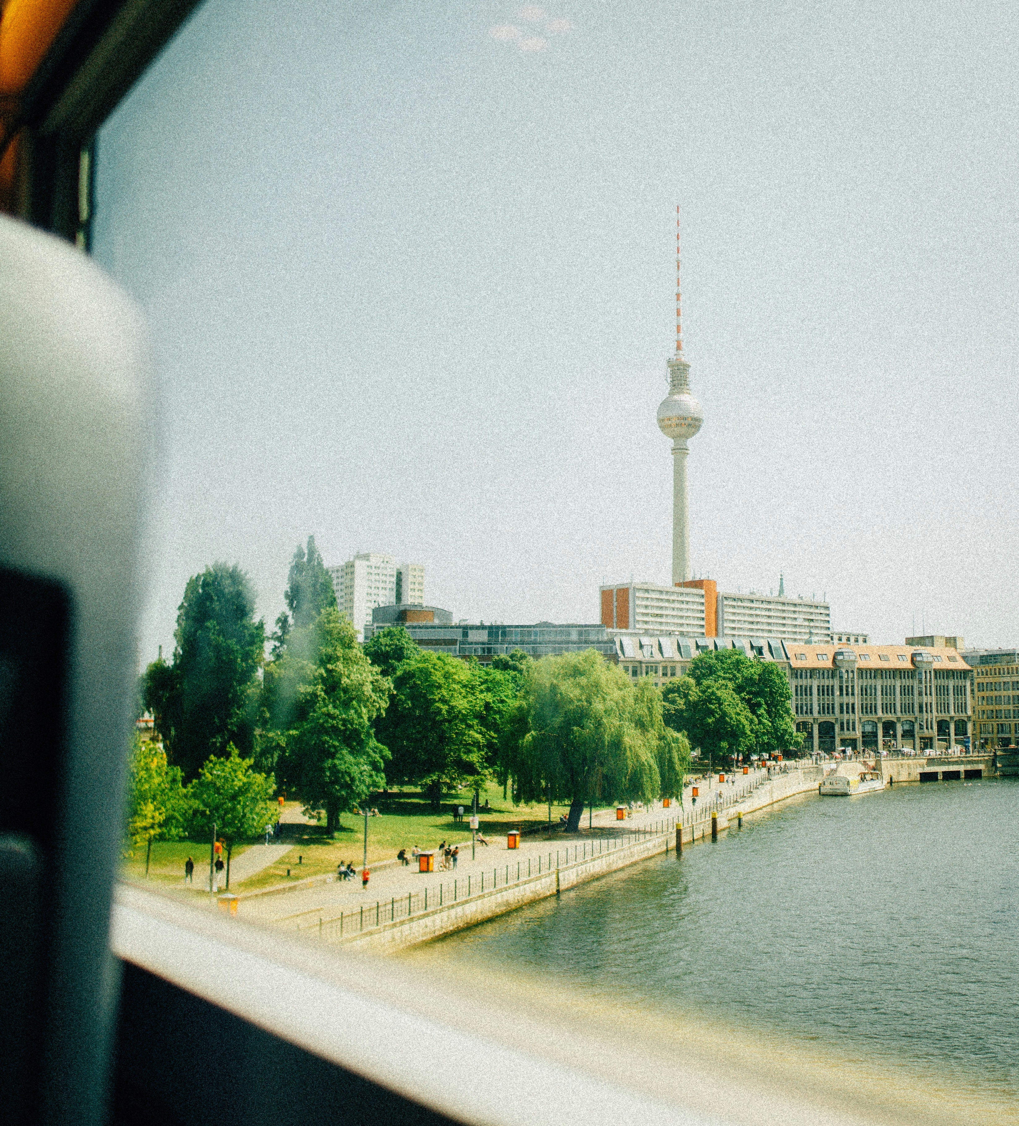 Berlin cityscape with fernsehturm, river, and green trees.