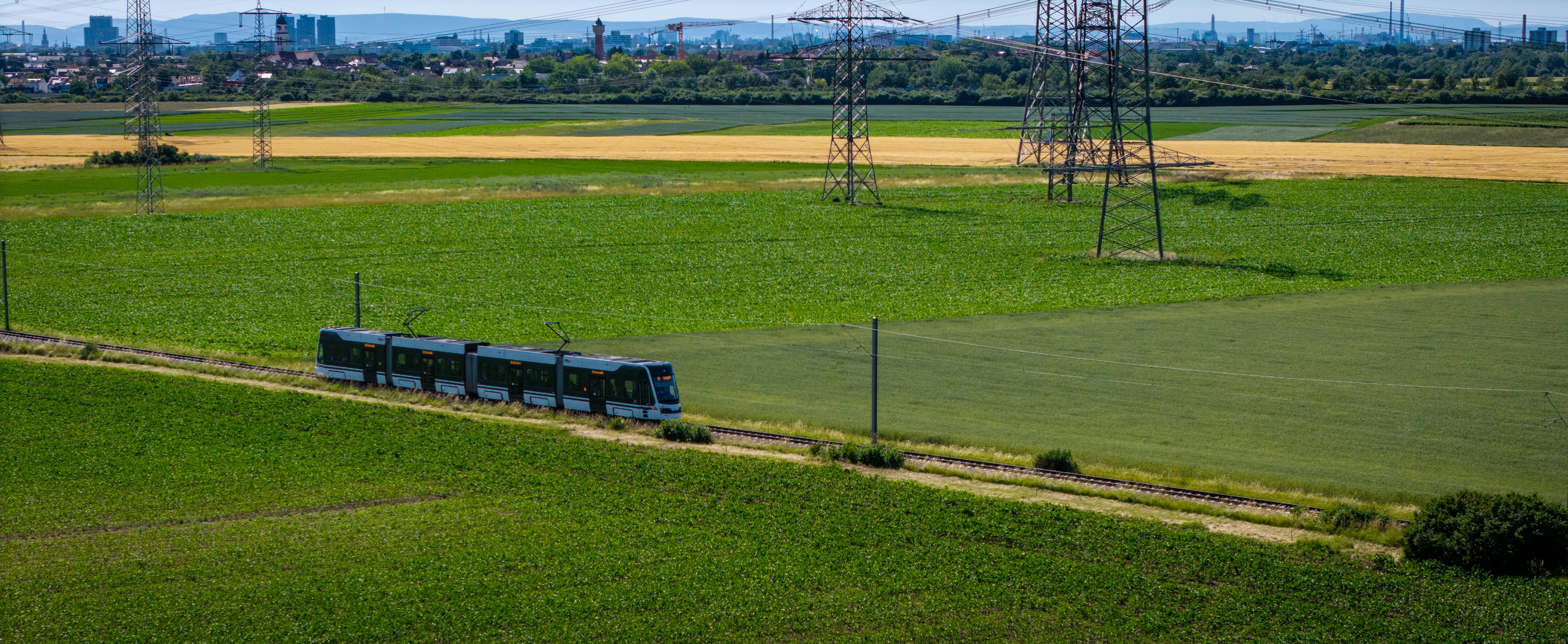 A tram moves through green fields under power lines.
