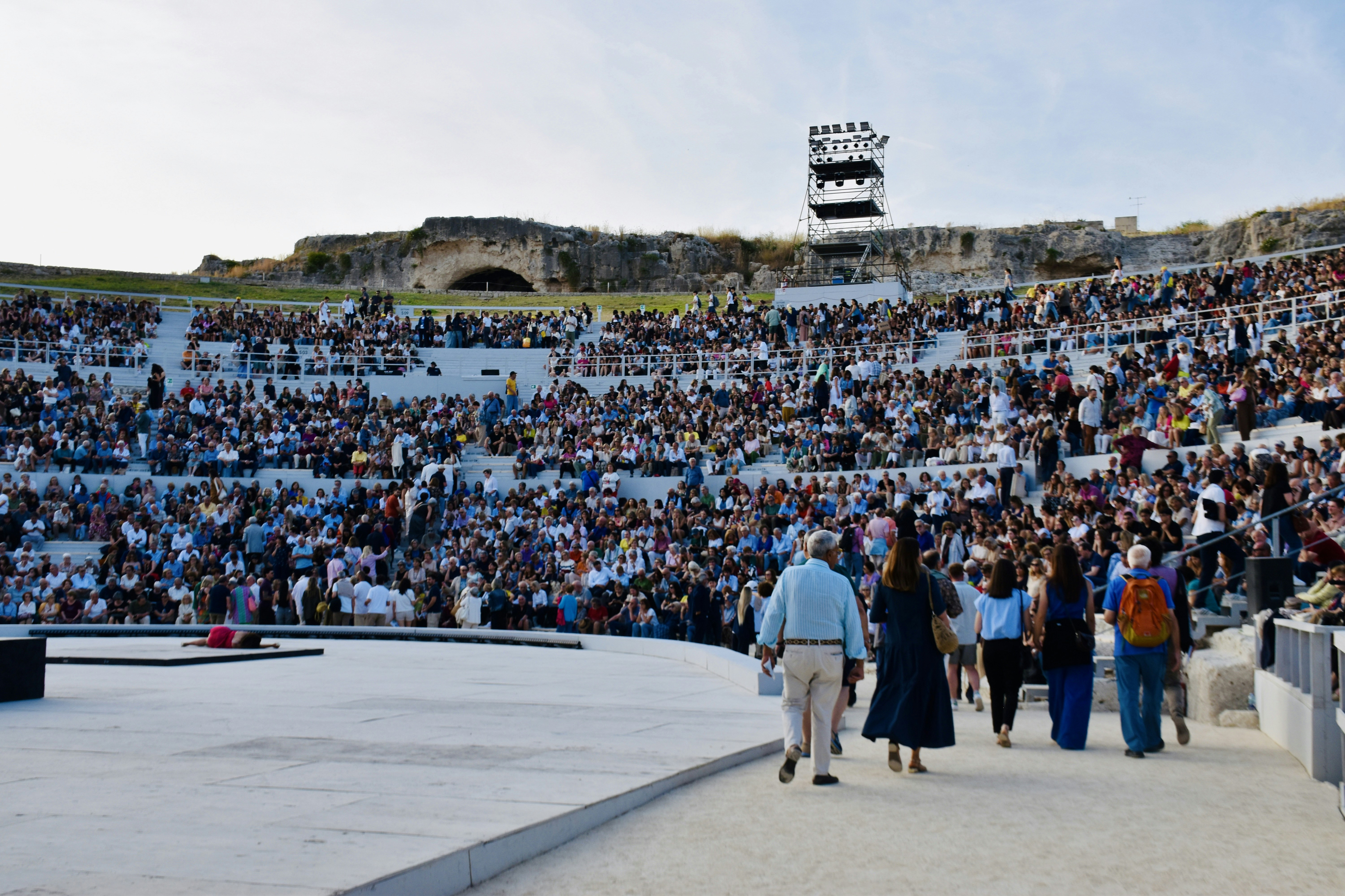 A large crowd gathers in an ancient amphitheater at sunset.