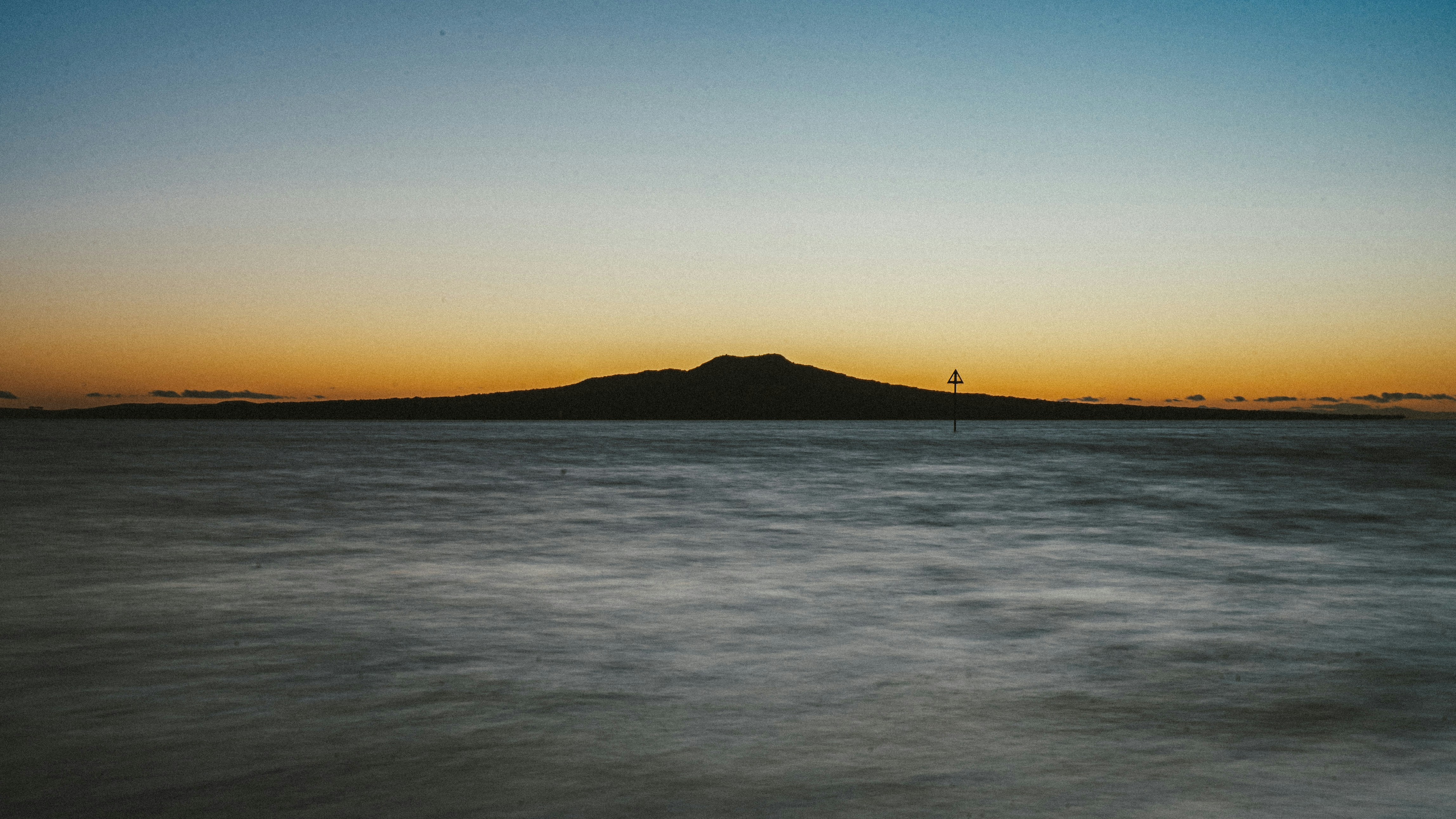 Siluet pulau yang jauh di atas air yang tenang saat matahari terbenam.