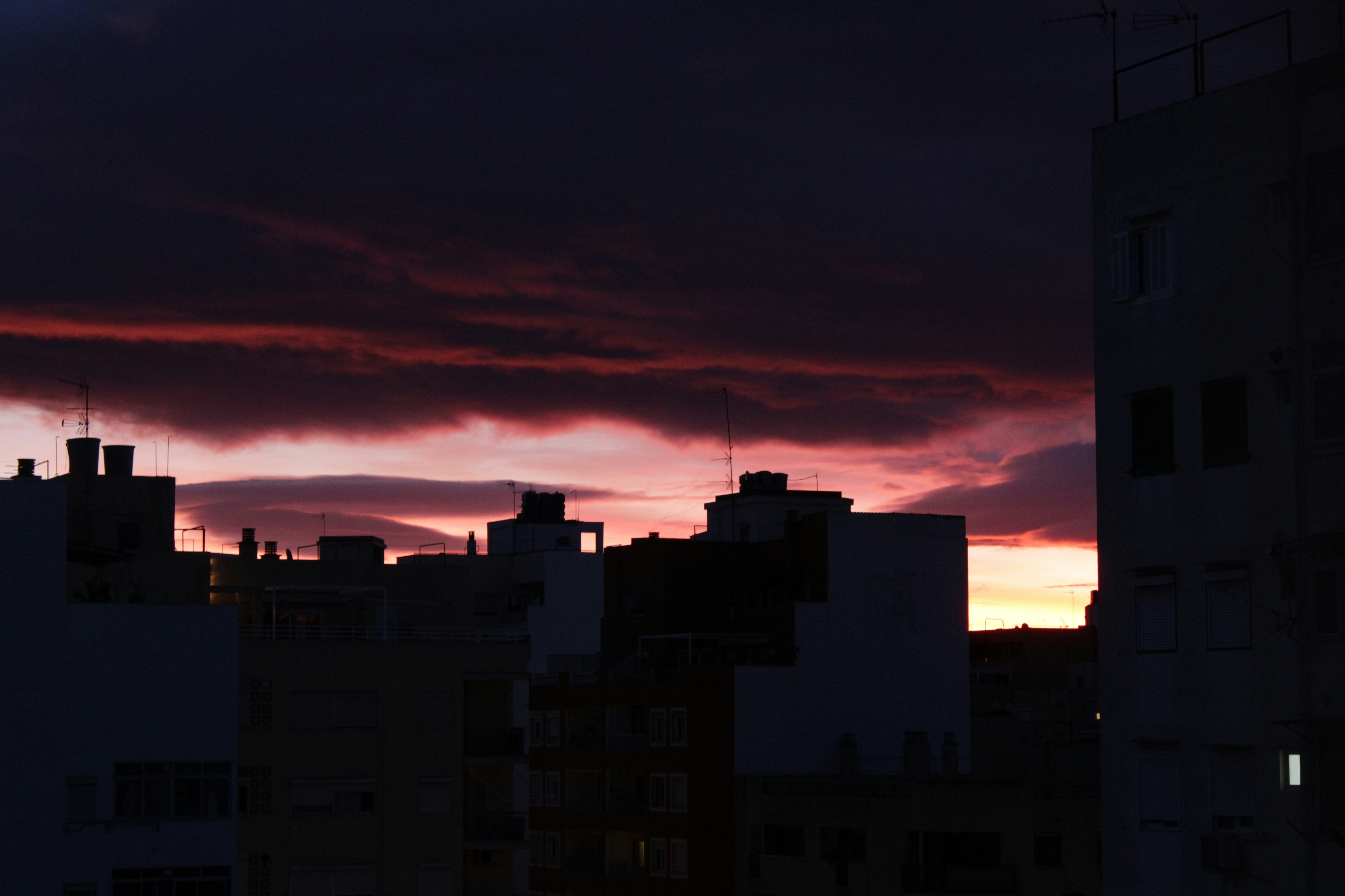 Dark city skyline against a vibrant, dramatic sunset sky.