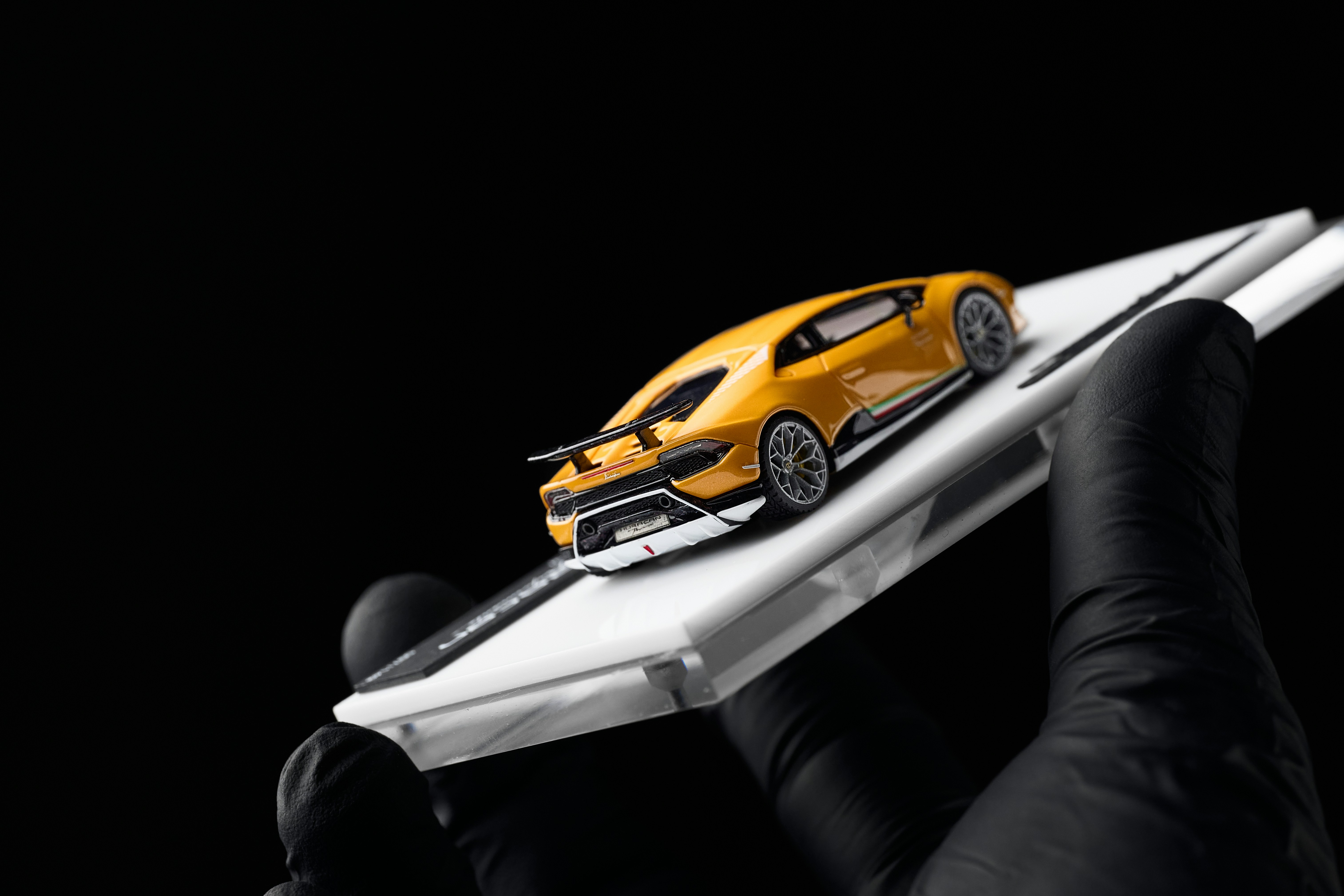 Yellow toy car on white smartphone held by gloved hand
