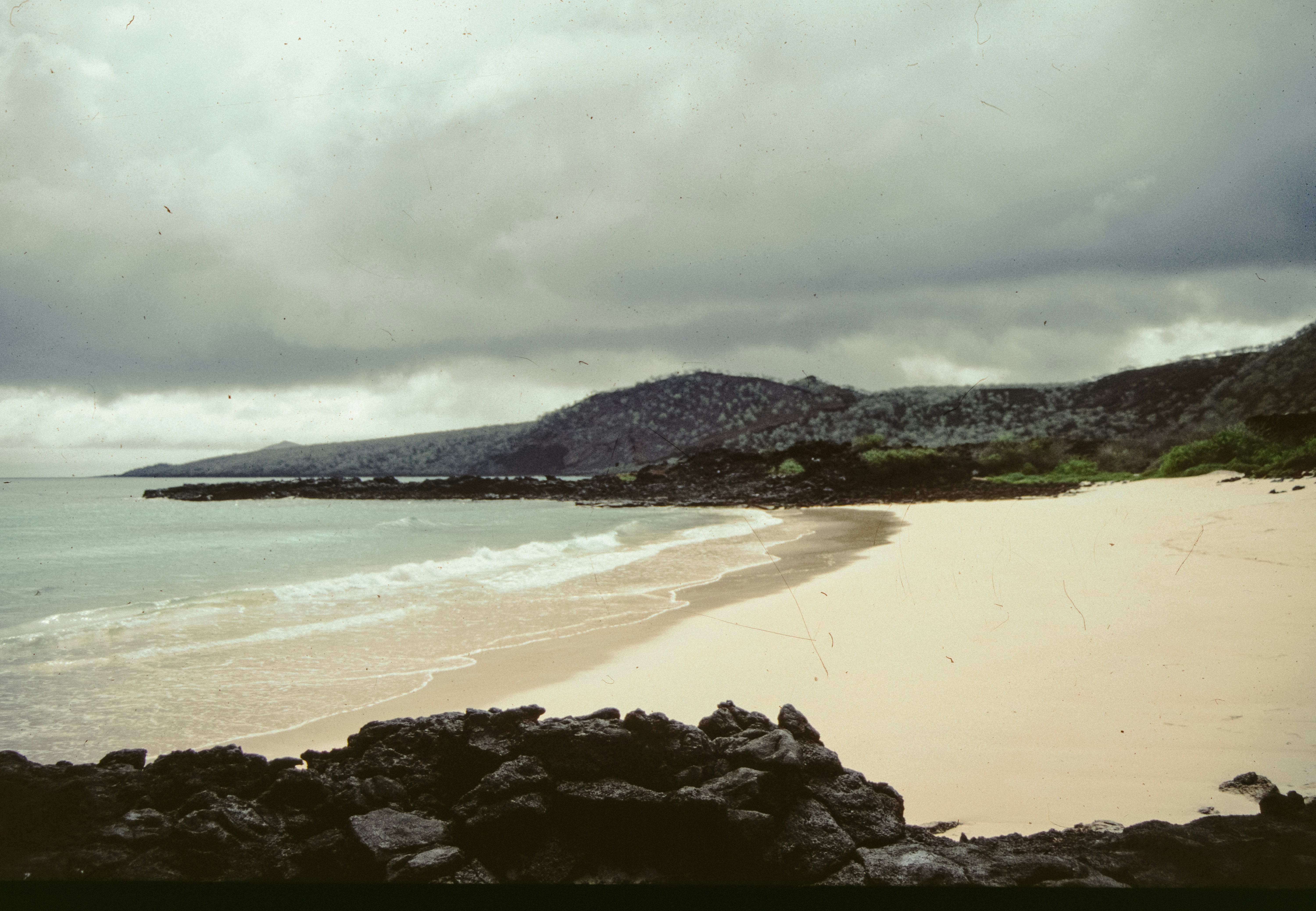 Ocean waves wash a sandy beach with rocky hills.