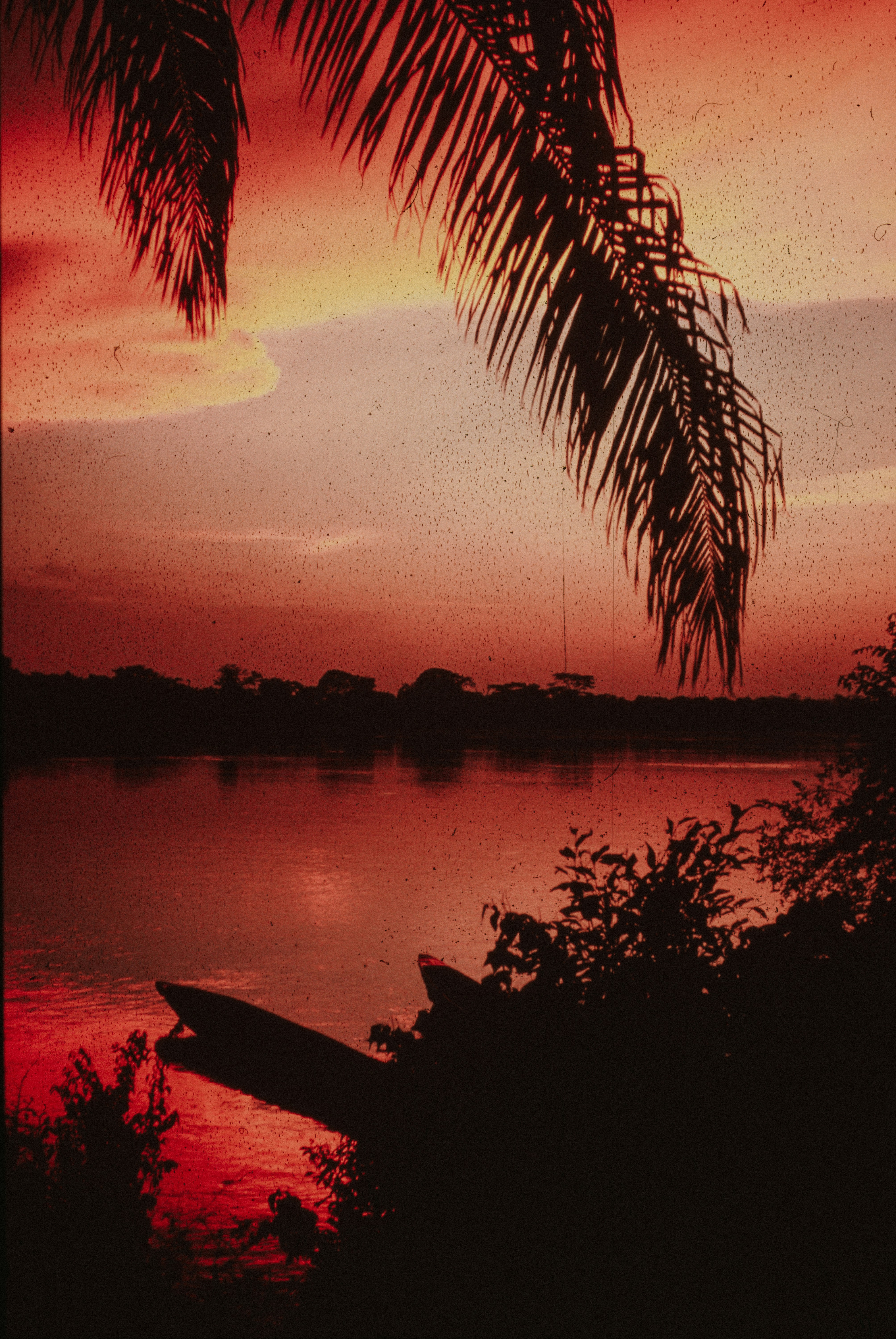 Red sunset over a calm river with a silhouetted boat.