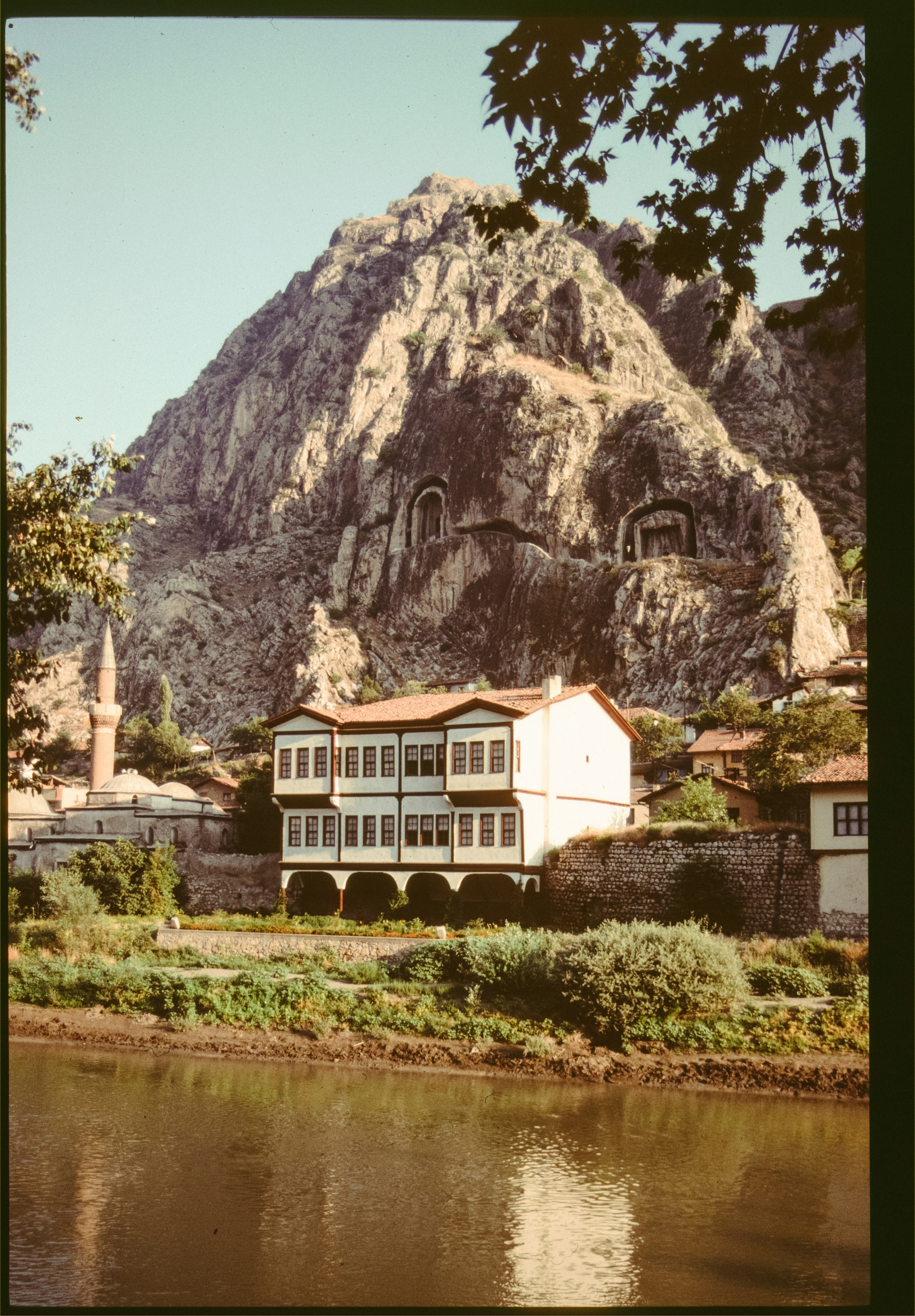 Traditional house by river with ancient carved mountain and mosque.