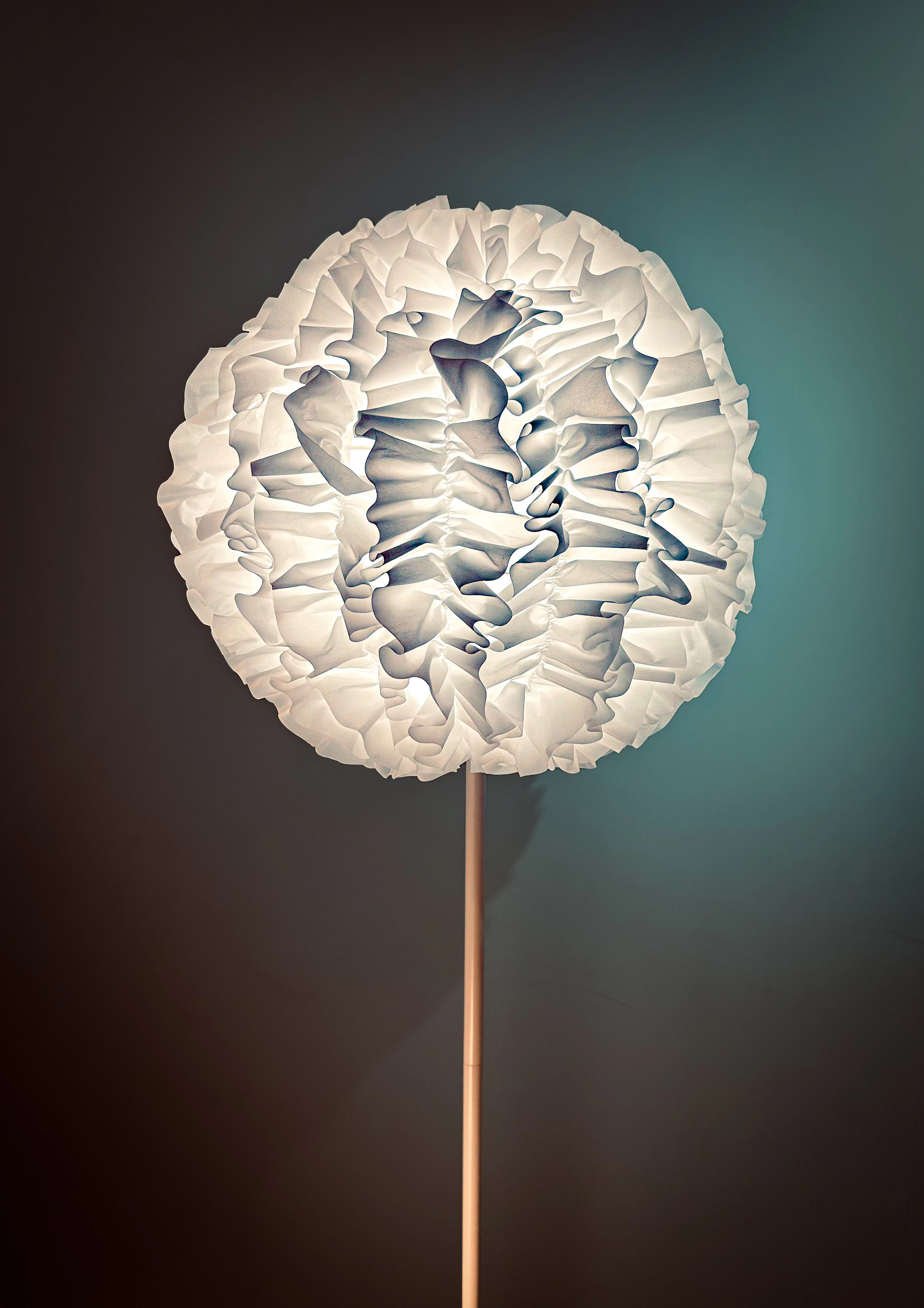 A white ruffled paper lantern lamp on a wooden stand.