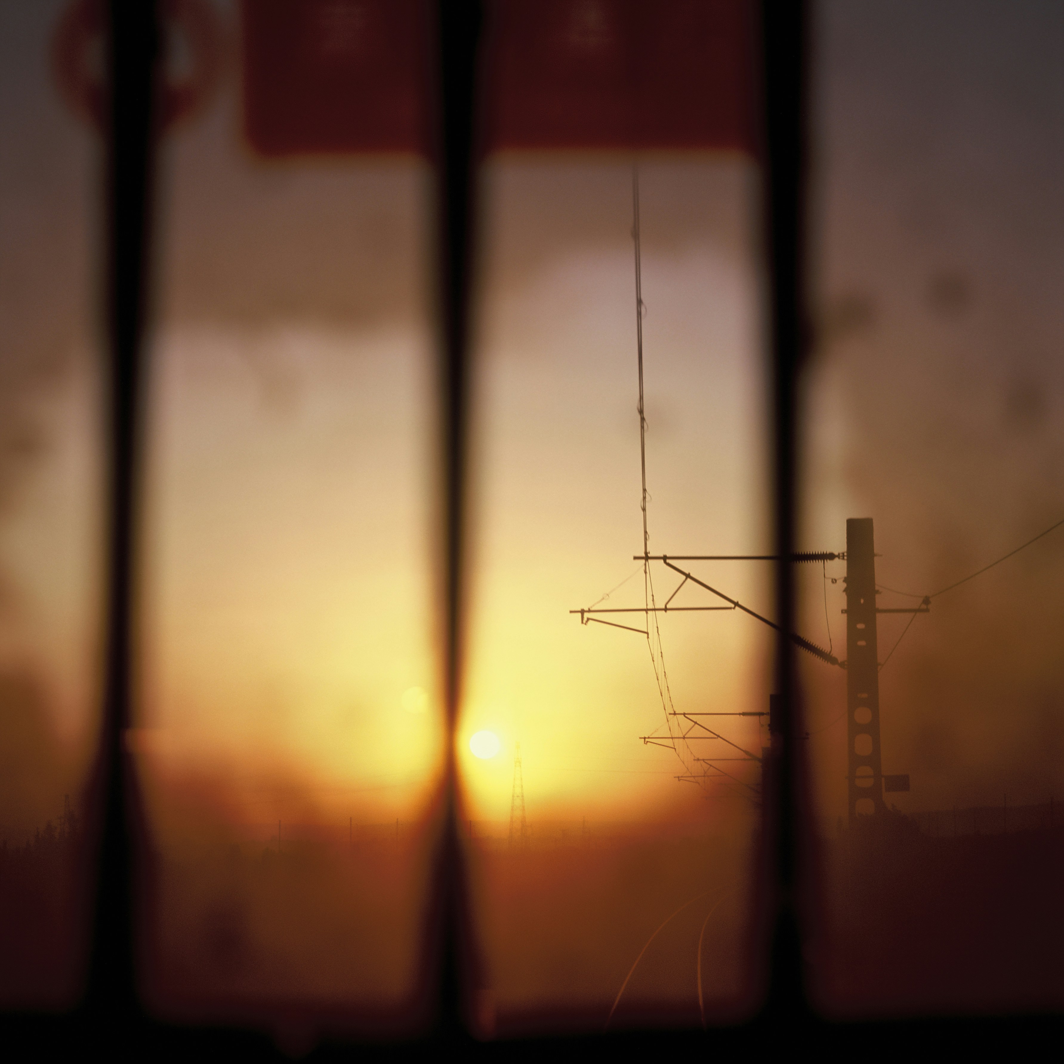 Warm sunset behind blurred vertical bars and industrial structures.
