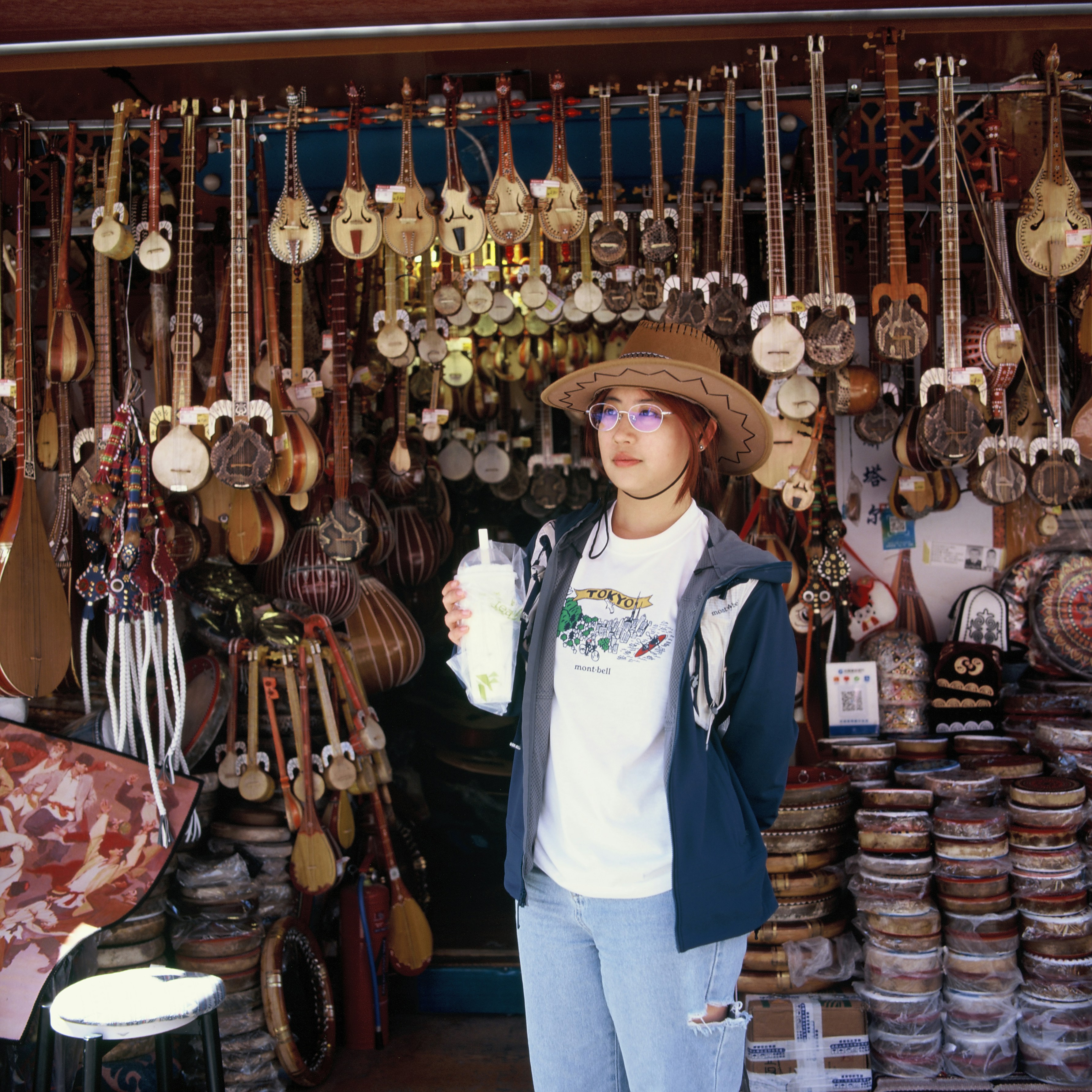 Young woman in hat holds drink amidst hanging musical instruments.