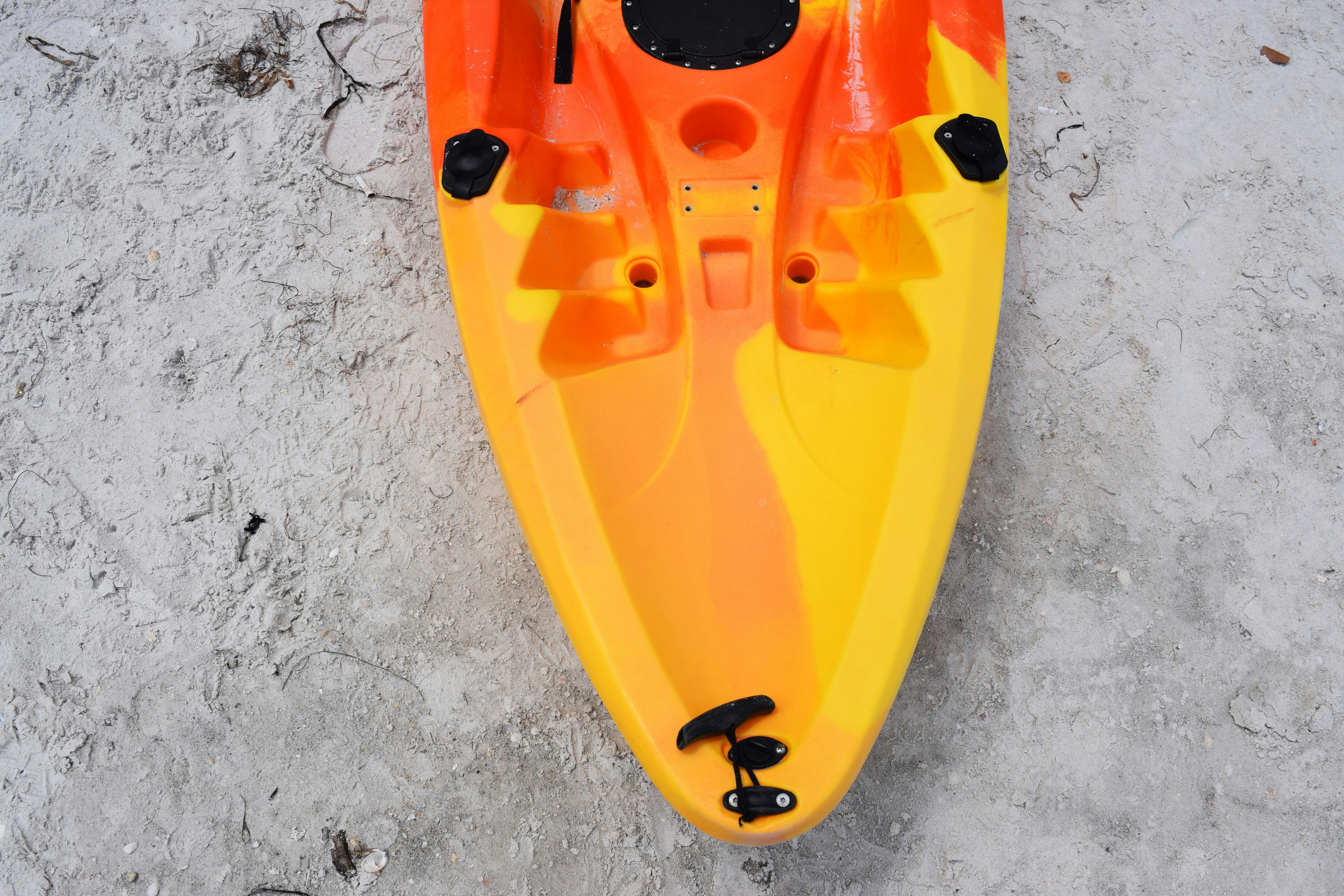 An orange and yellow kayak rests on a sandy beach