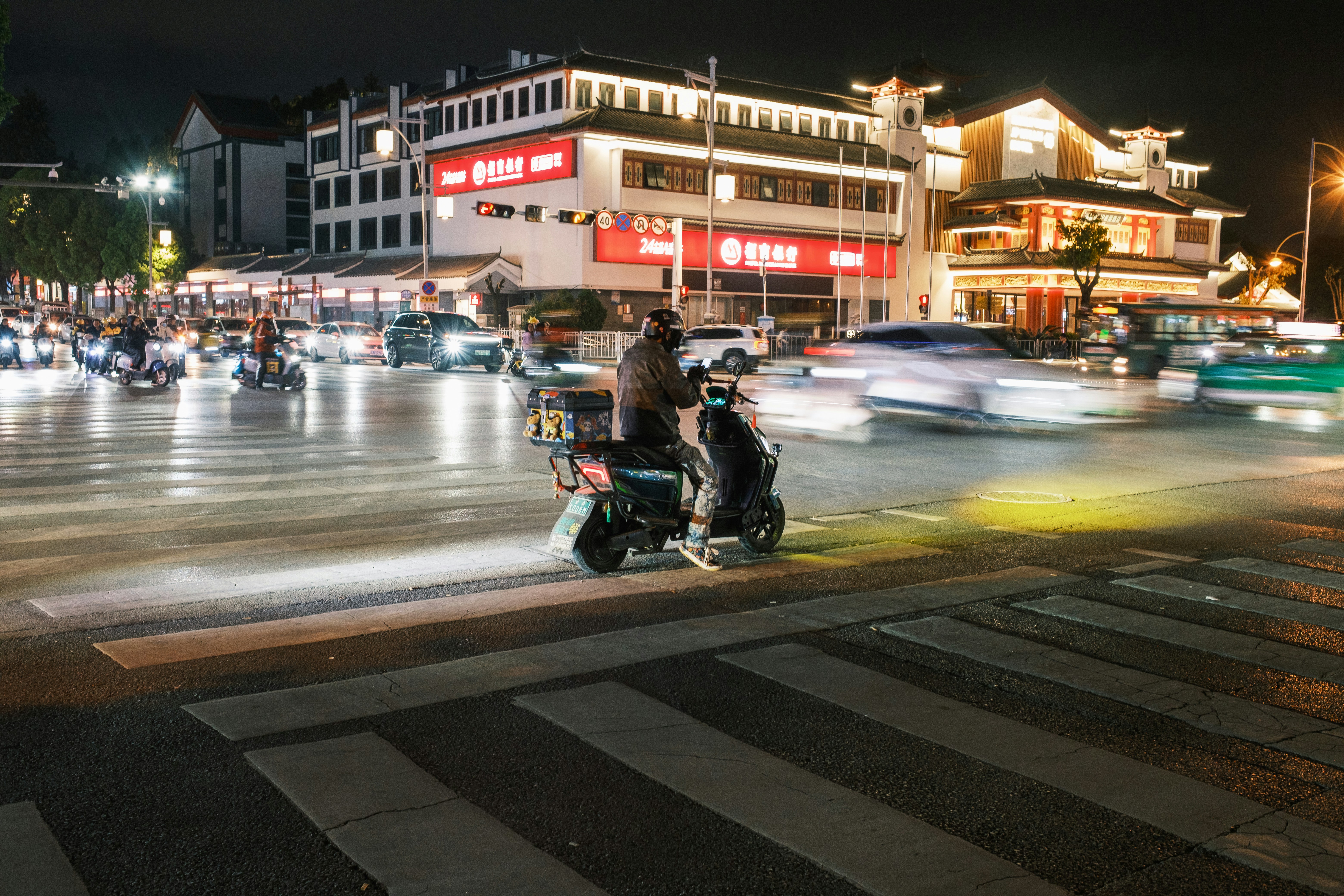 City street at night with a scooter and blurred traffic.