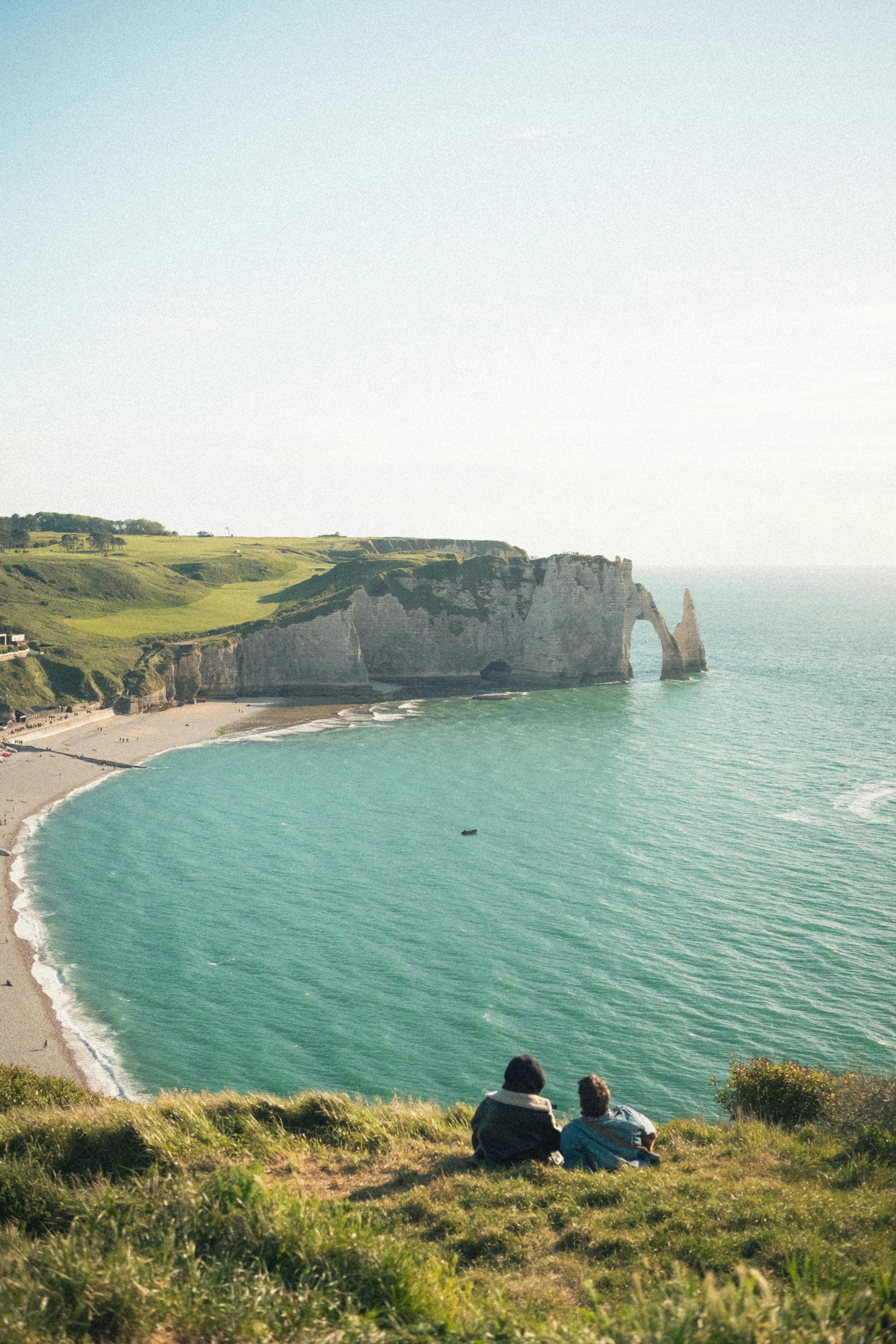 Two people watching the ocean from a grassy cliff.