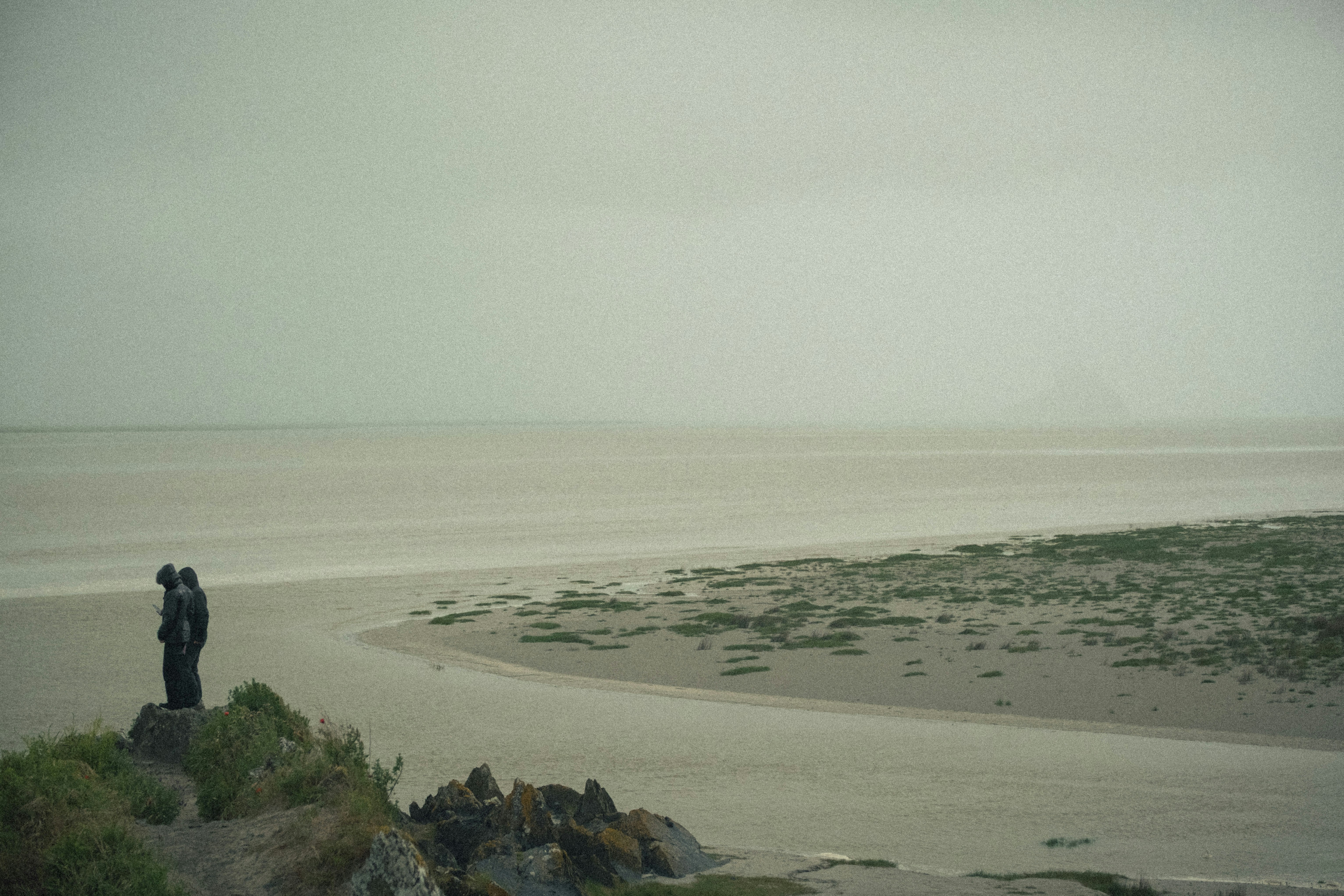 Two people on a cliff overlooking a vast, overcast bay.