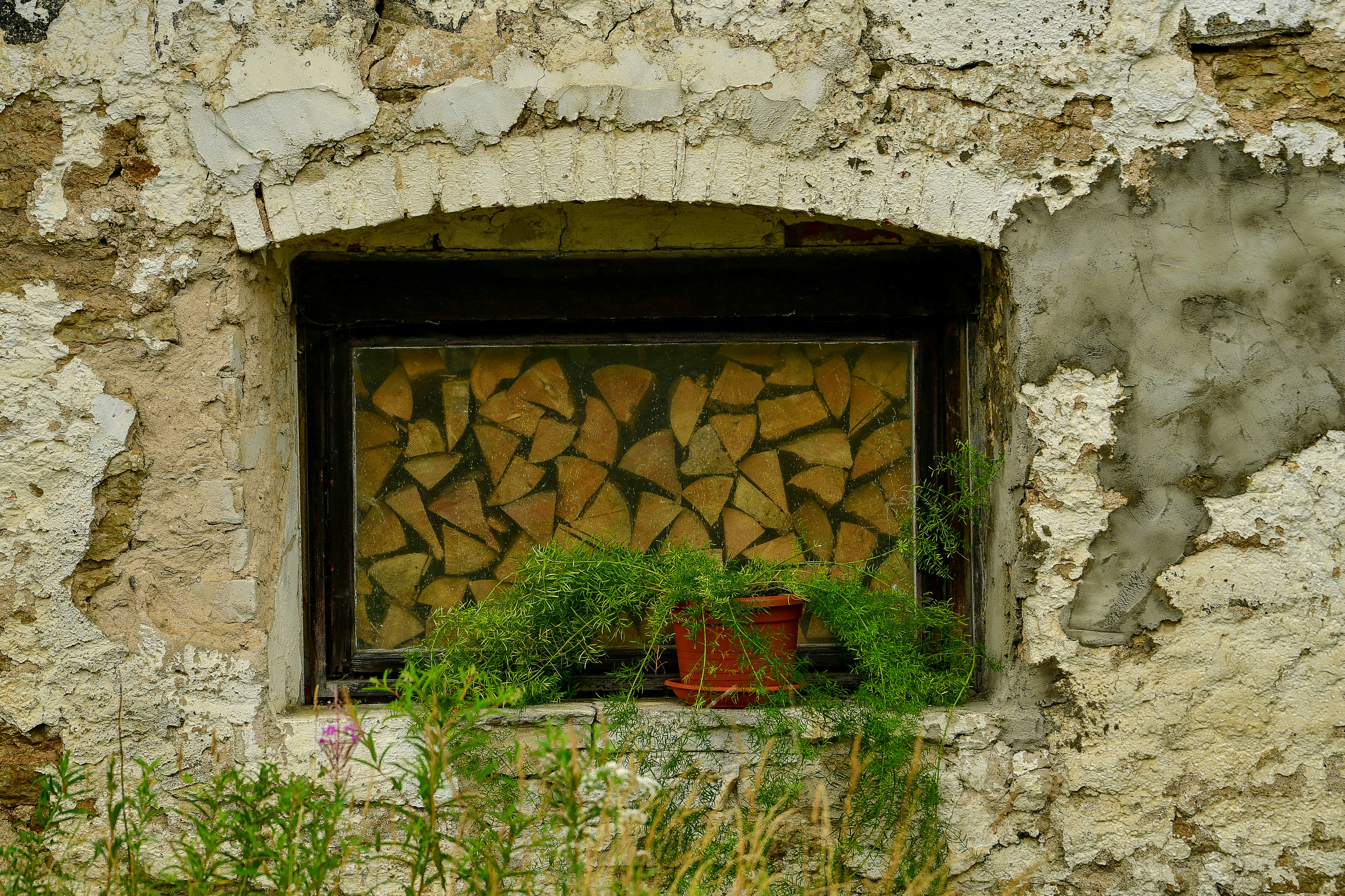 Muro di pietra consumato dal tempo con legna impilata dietro una finestra.