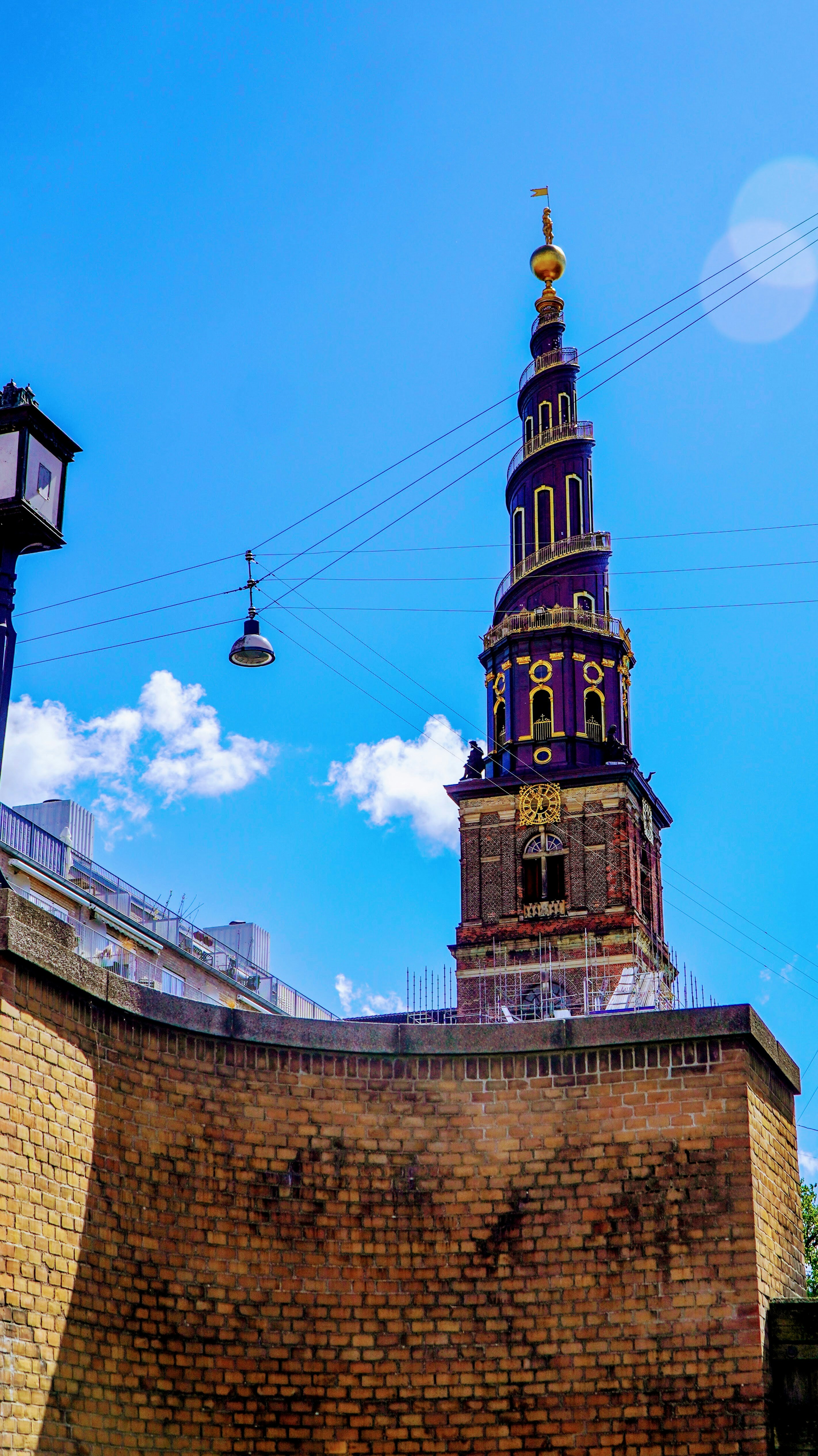 Ornate spiral church spire rises above a brick wall.