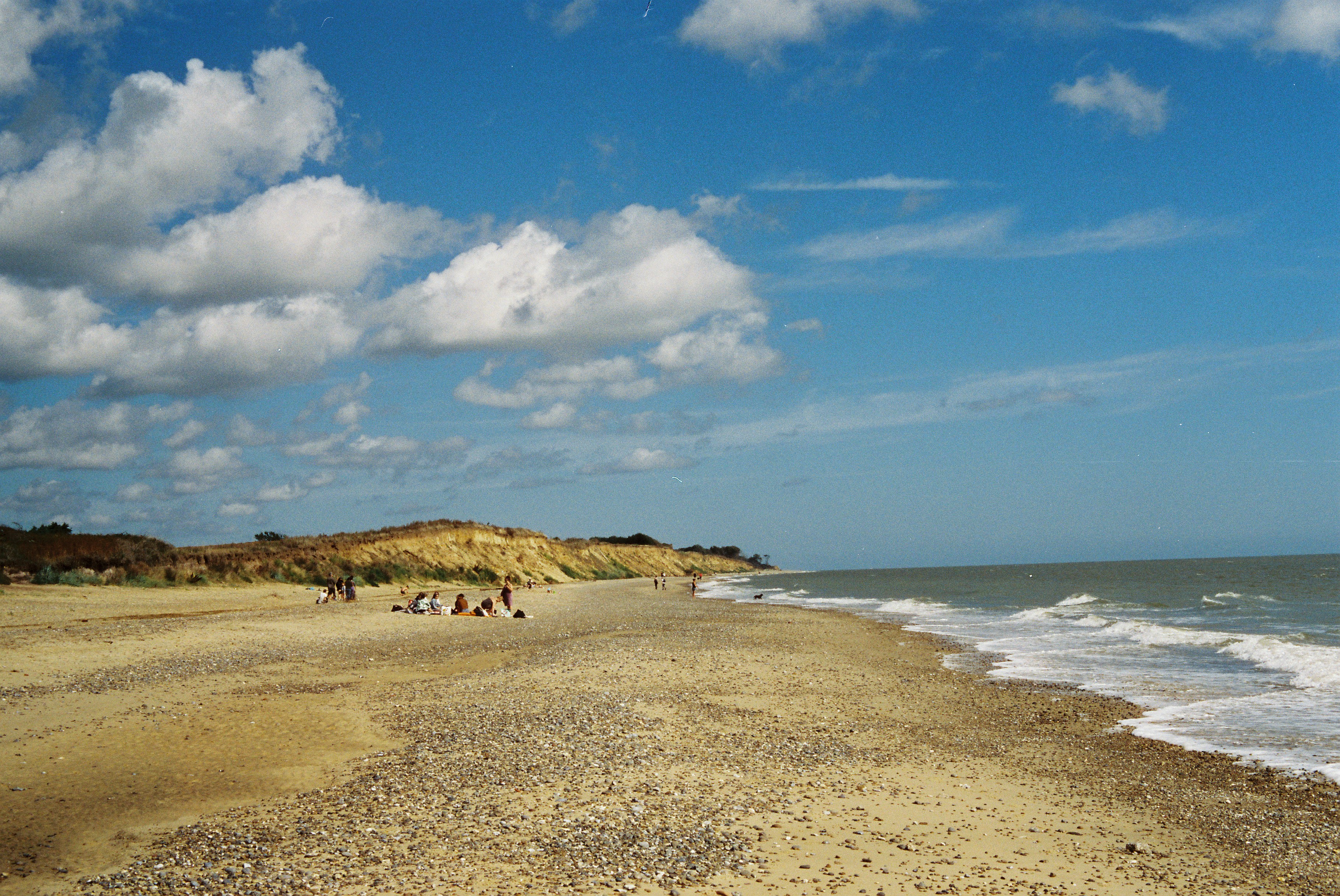 Sandy beach, ocean waves, and cliffs under a blue sky.