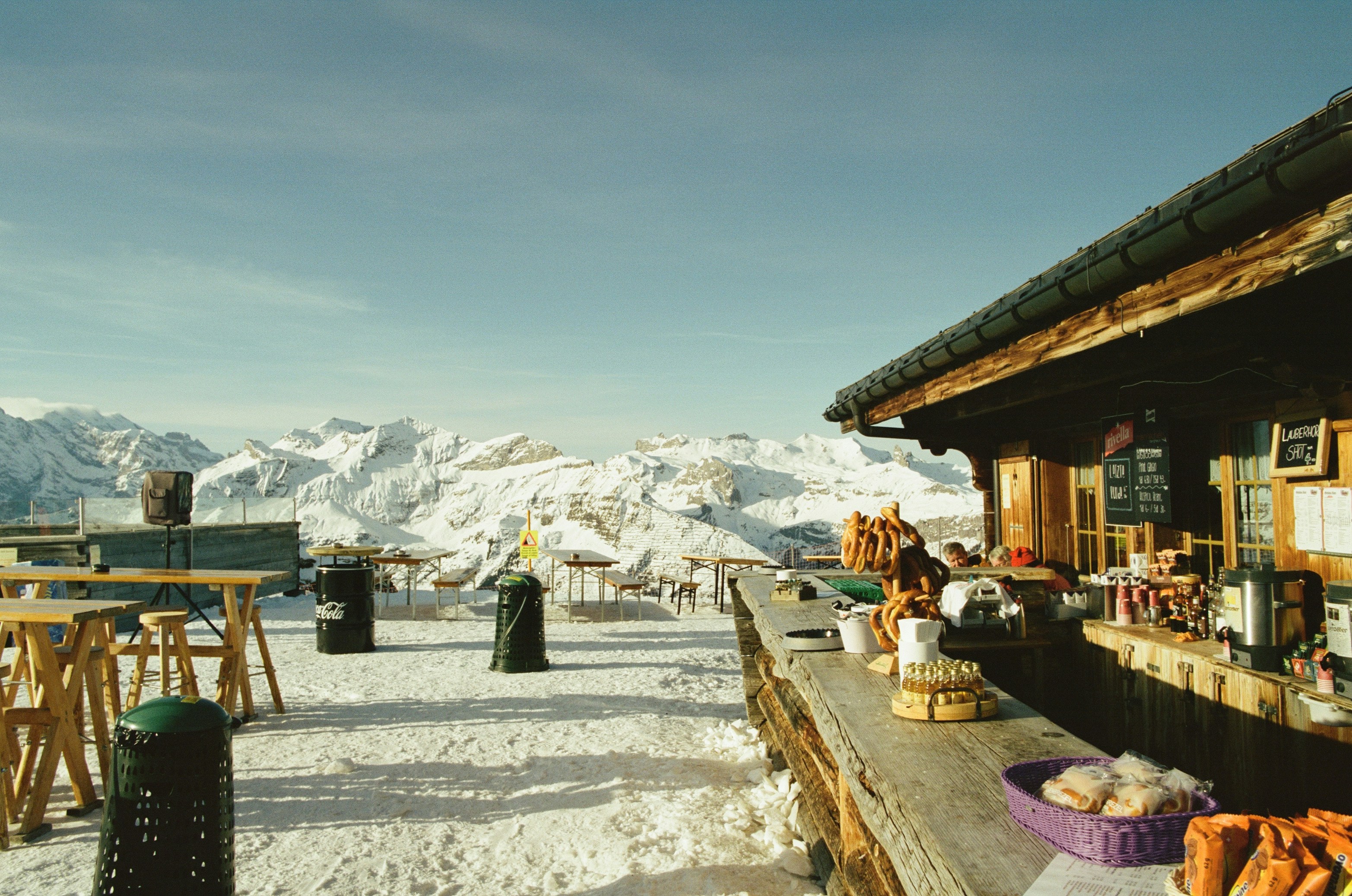 Sunny mountain hut bar with snowy peaks and clear sky.