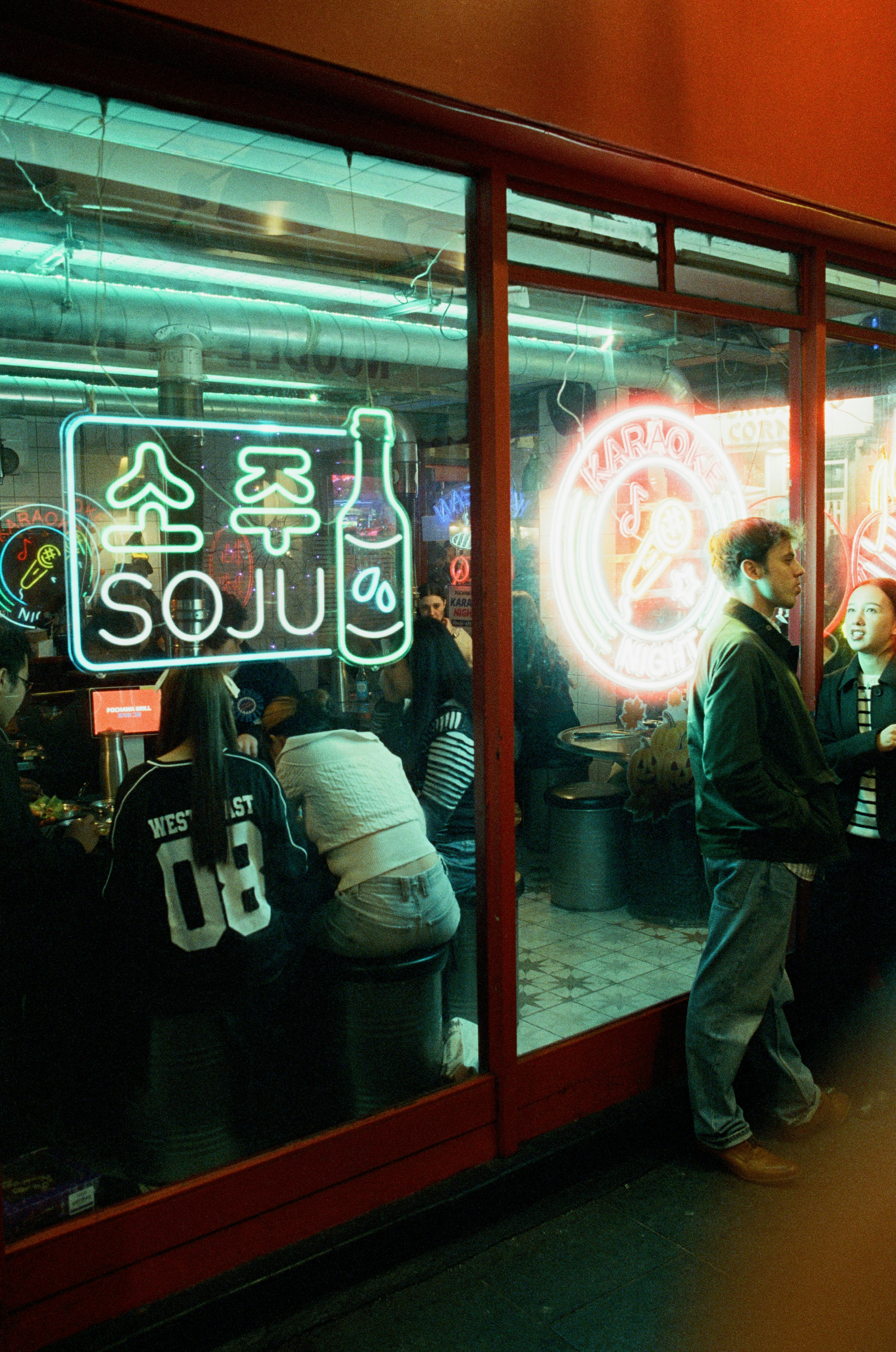 People inside a bar with neon "soju" sign at night