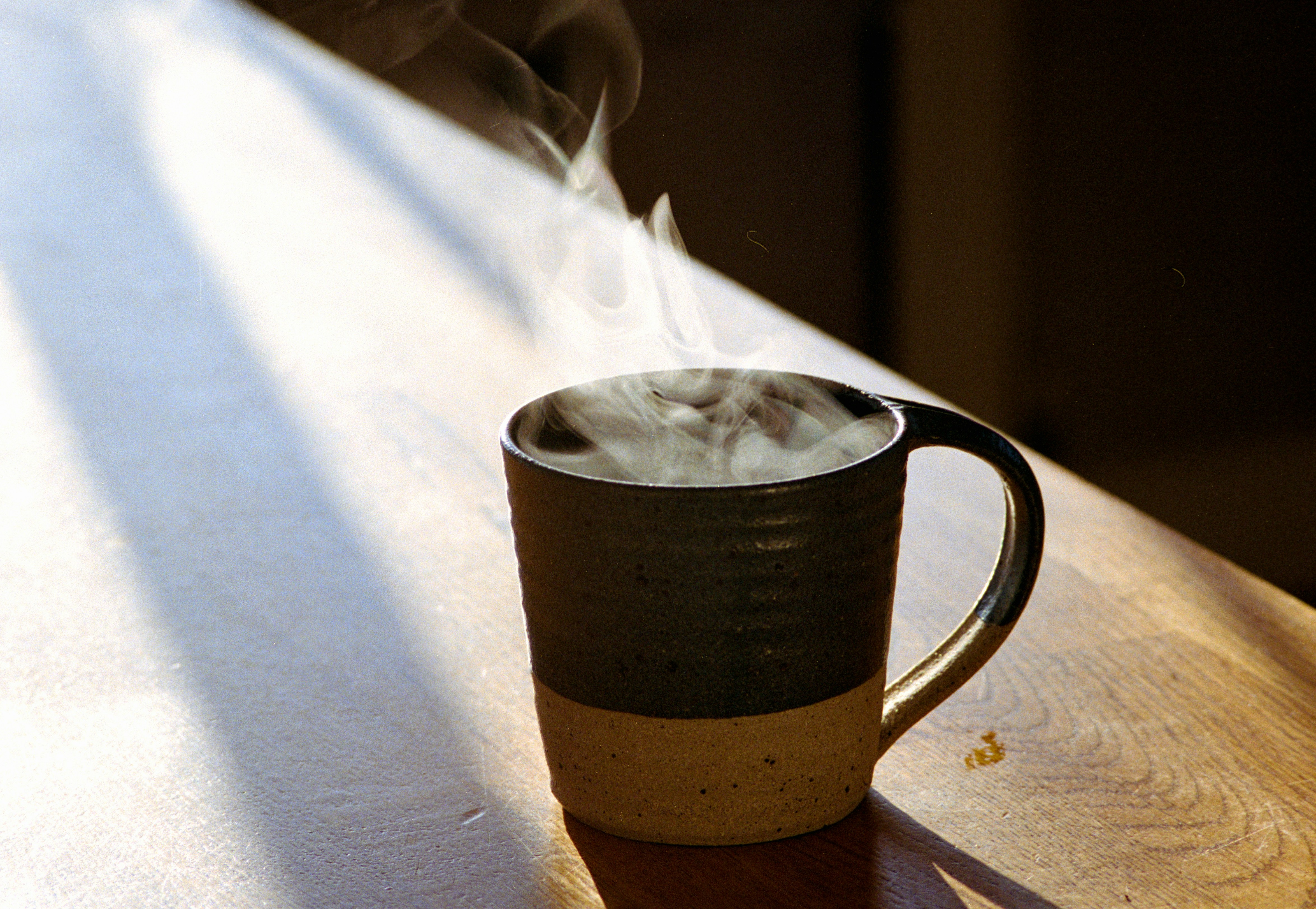 A steaming mug on a sunlit wooden surface.