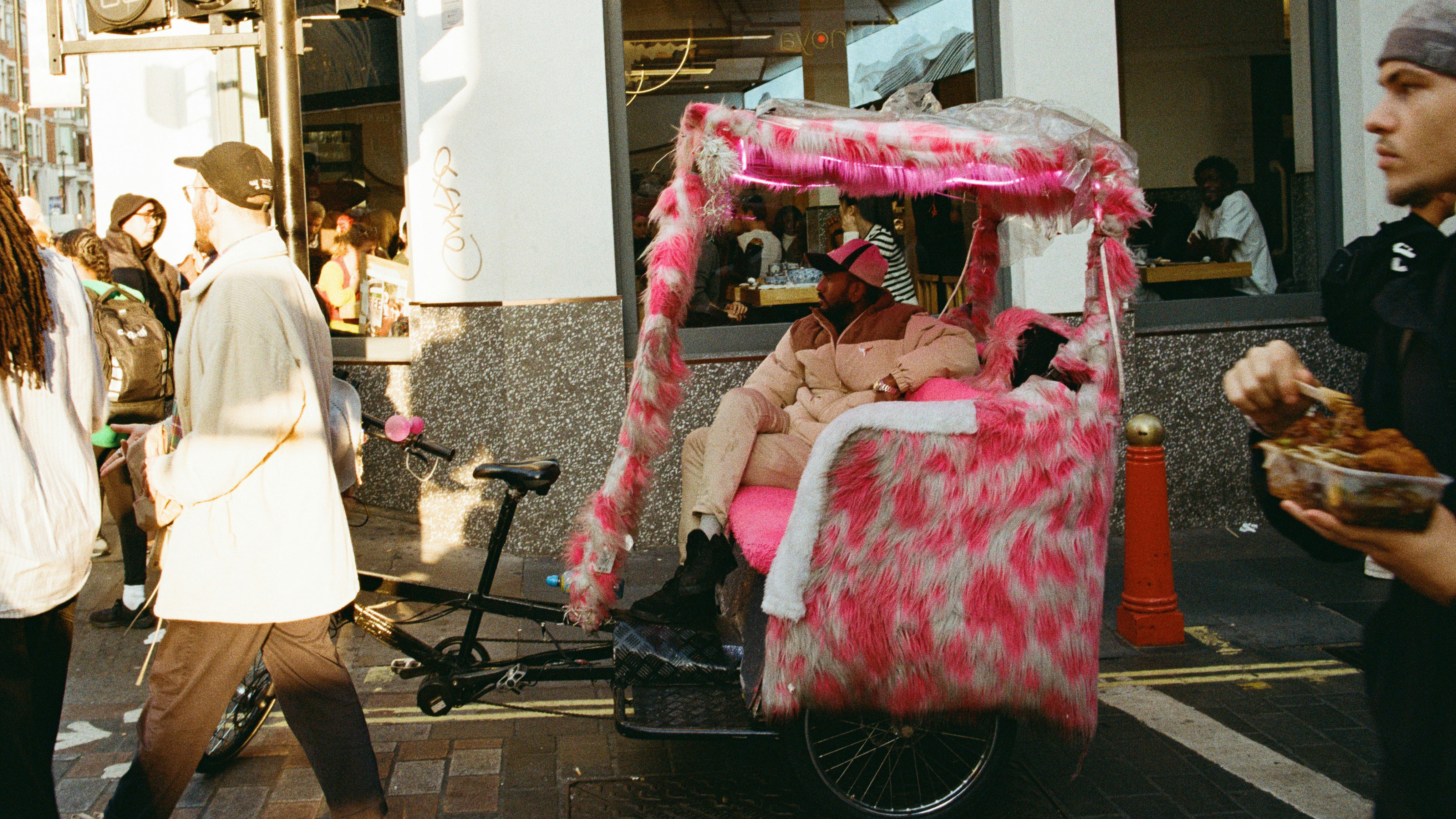 A pink rickshaw with a passenger on a busy street.