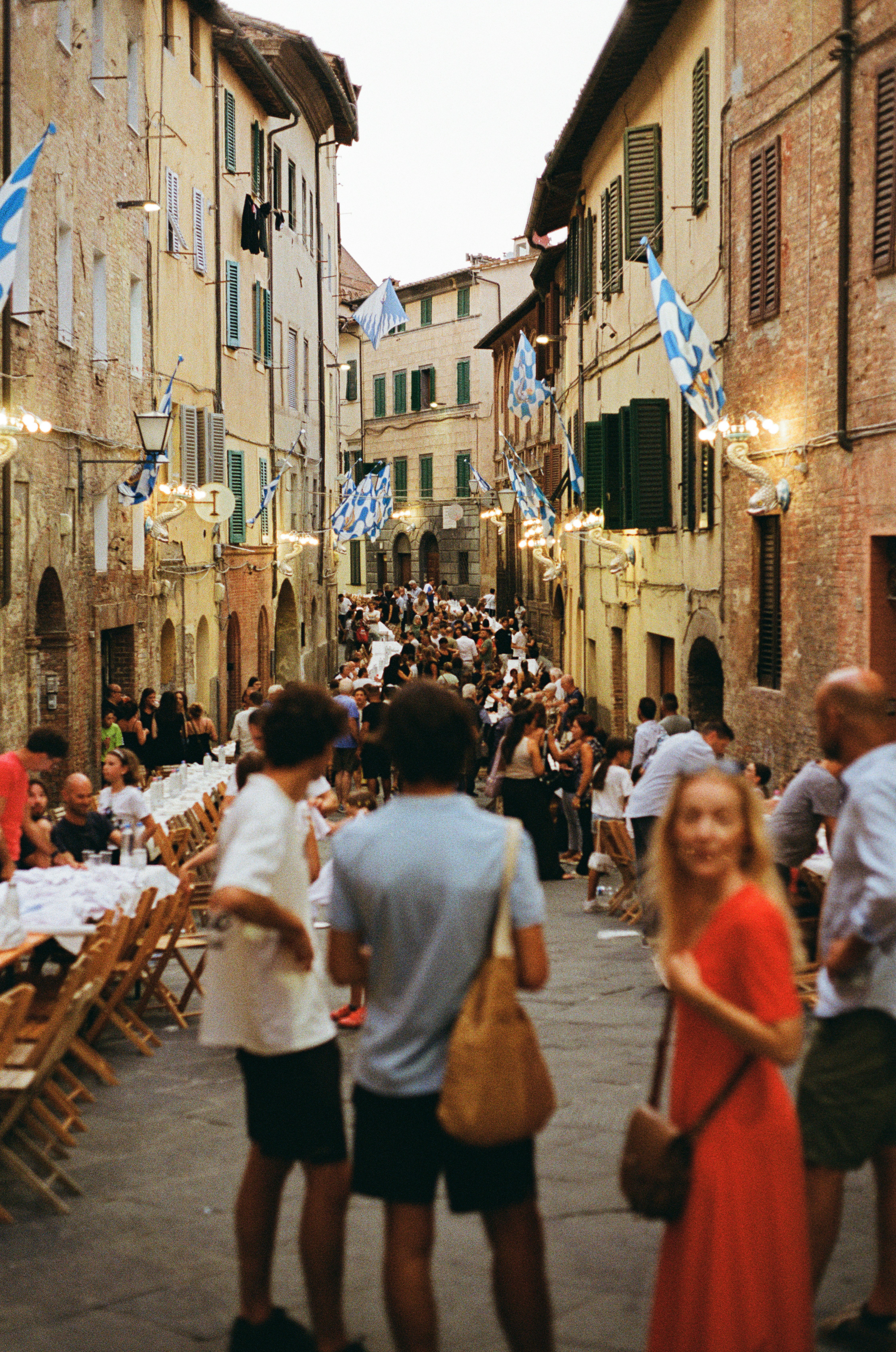 Folla si riunisce a lunghi tavoli durante una festa di strada all'aperto.