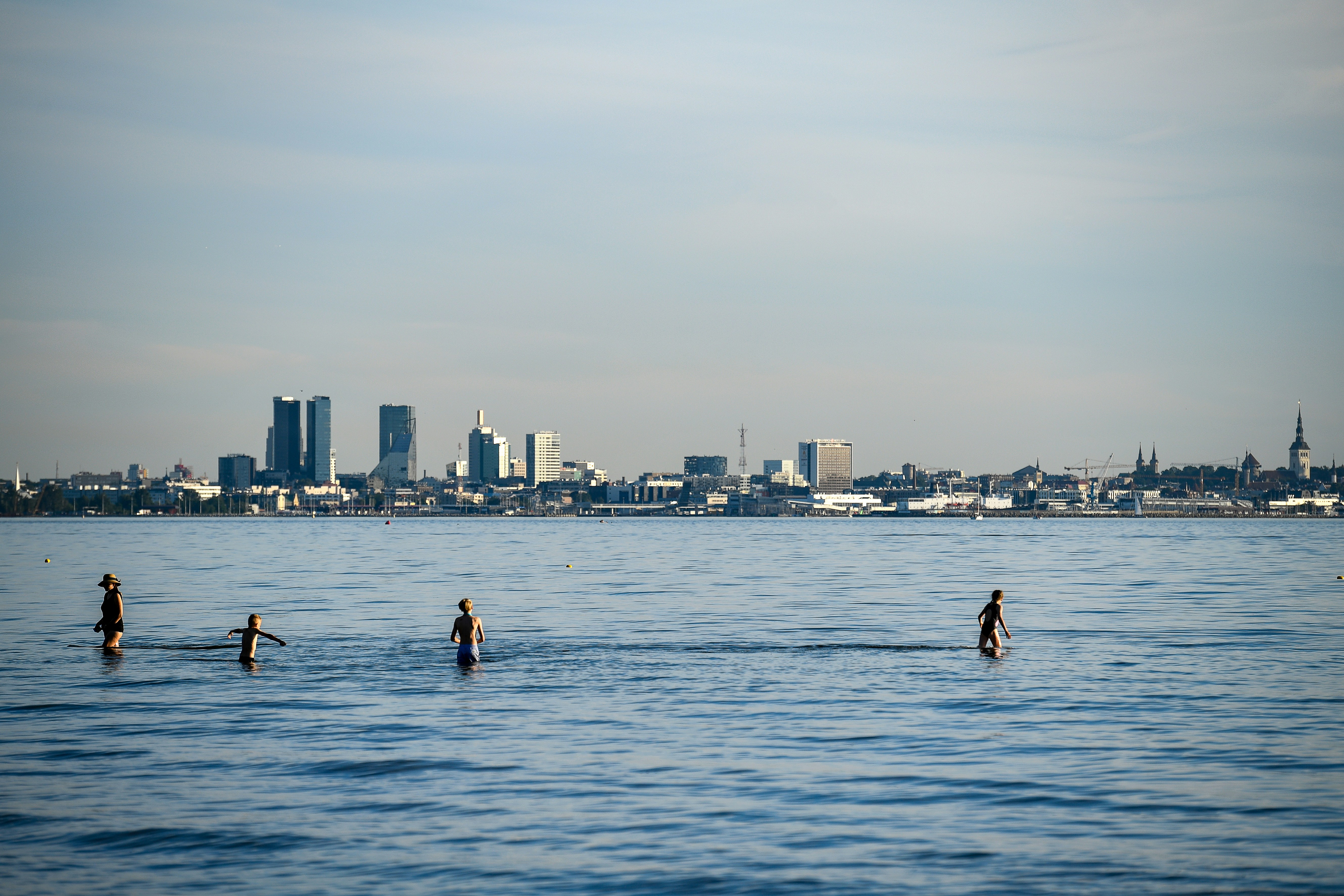 Persone che guadano nel mare con lo skyline della città lontano.