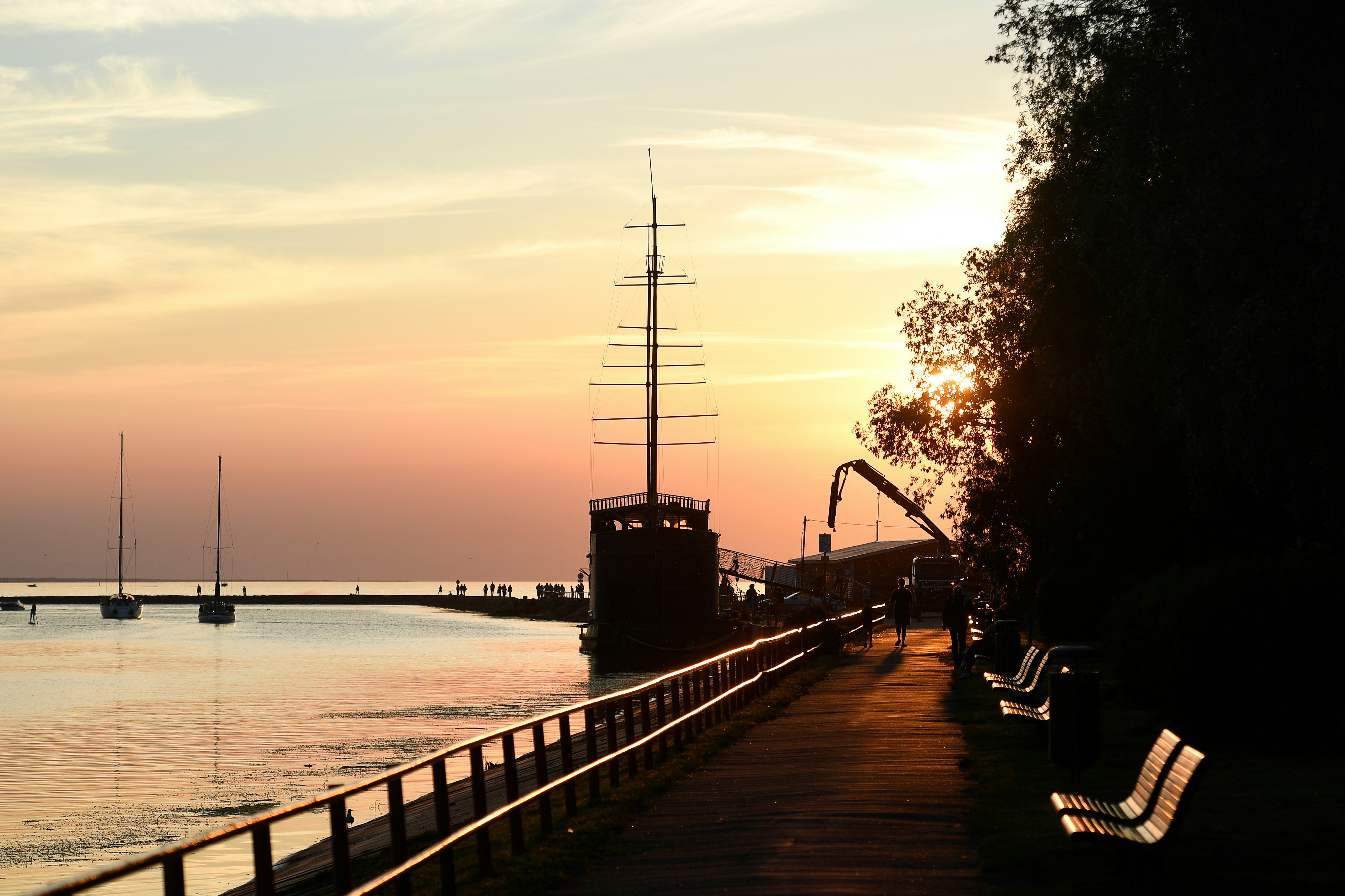 Il tramonto dorato illumina una nave, un molo e le panche sul lungomare.