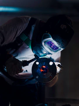 A welder works on a metal object with bright sparks.