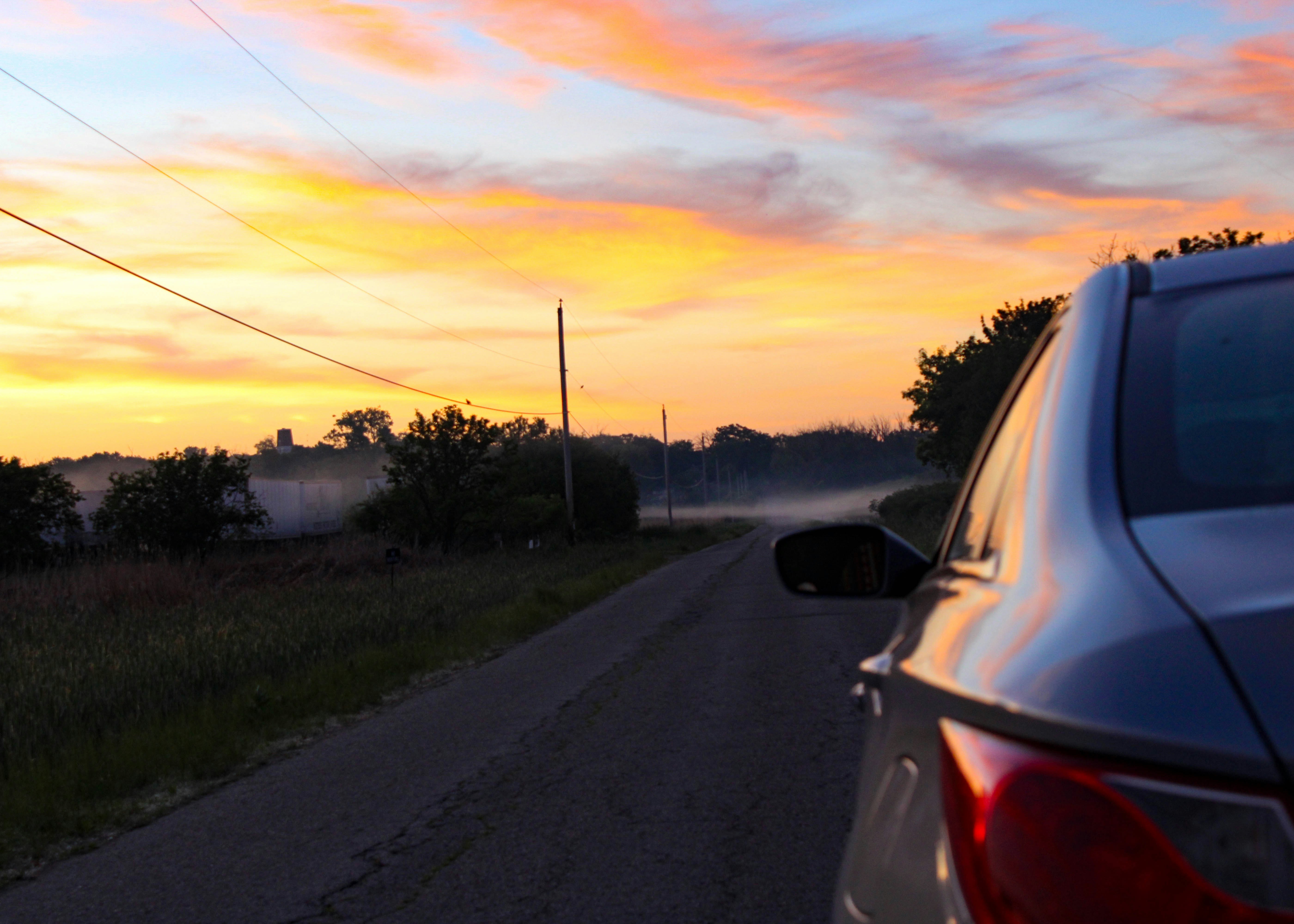 Car on a rural road at a vibrant sunset.