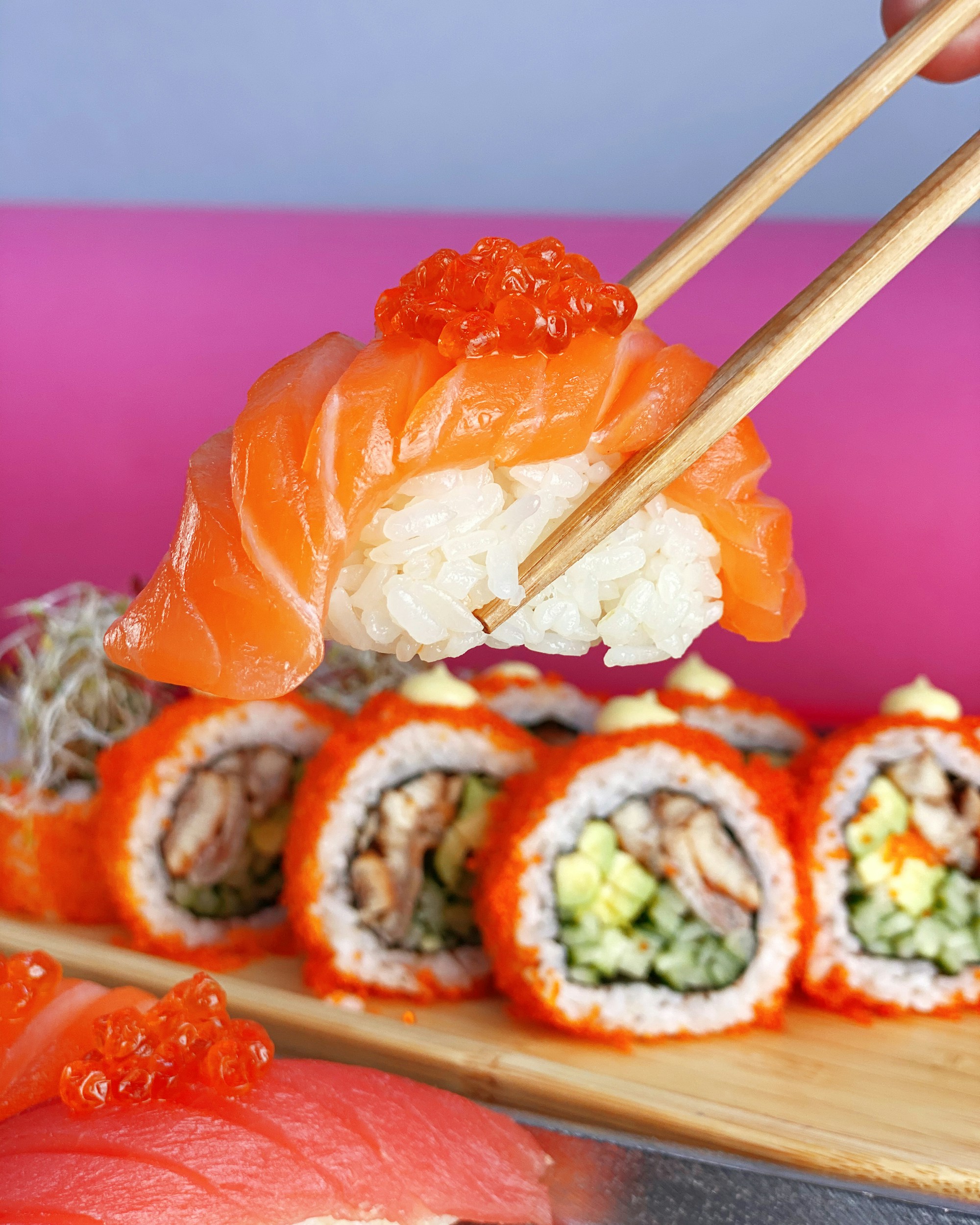 Chopsticks holding salmon sushi with roe over other sushi rolls