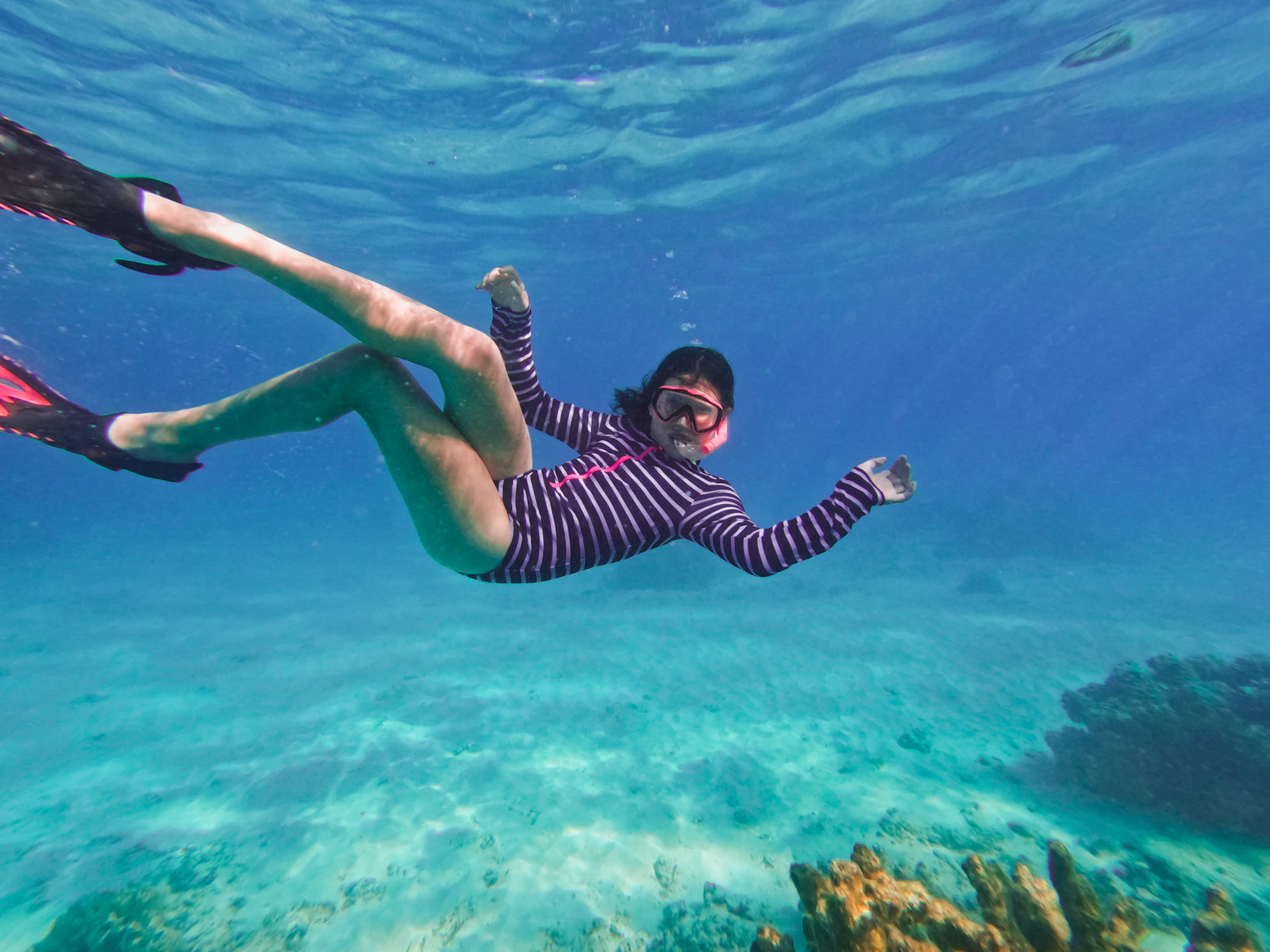 Snorkeler moving through clear blue water above a coral reef