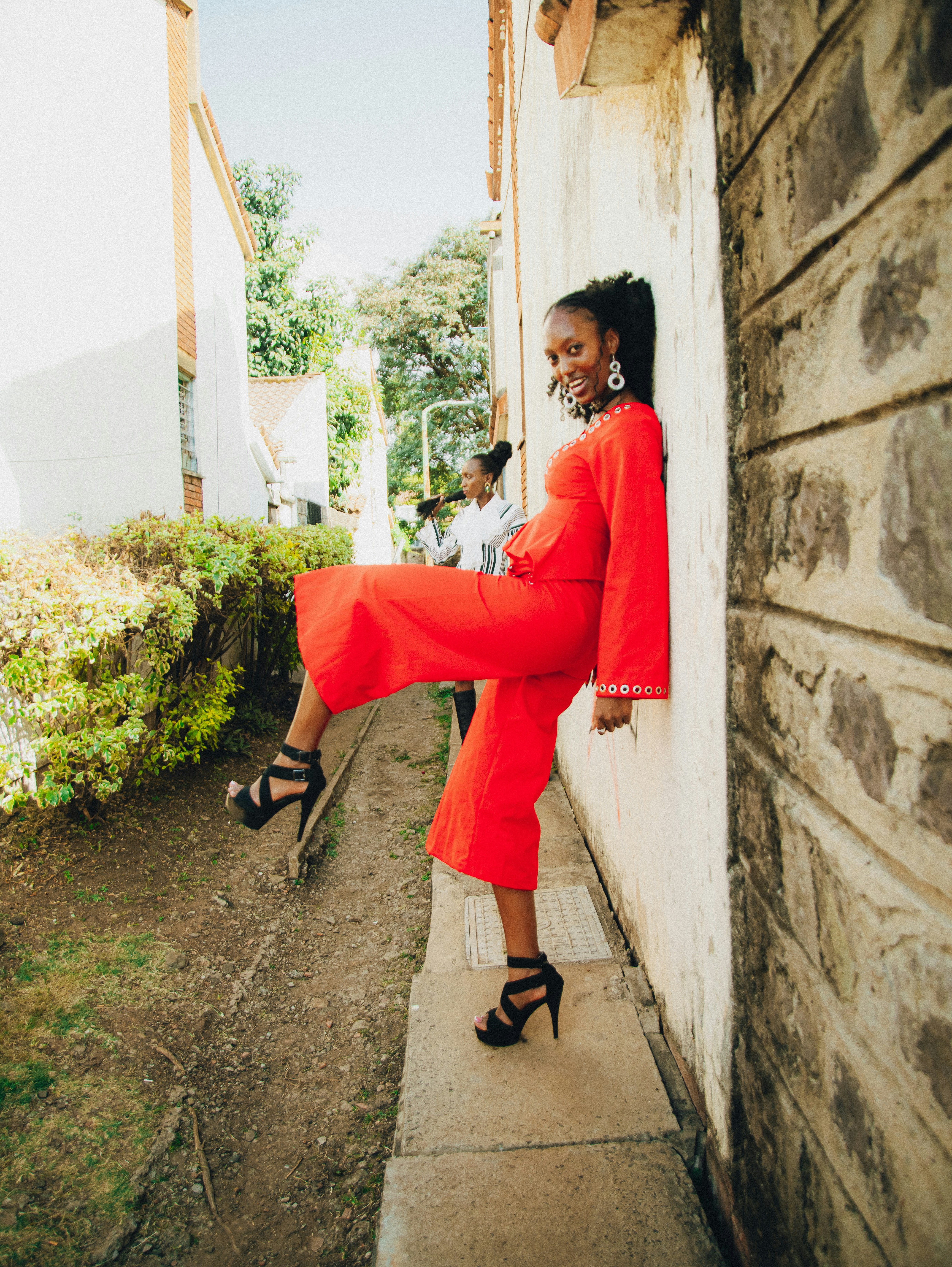 Young woman in red jumpsuit posing against a wall.