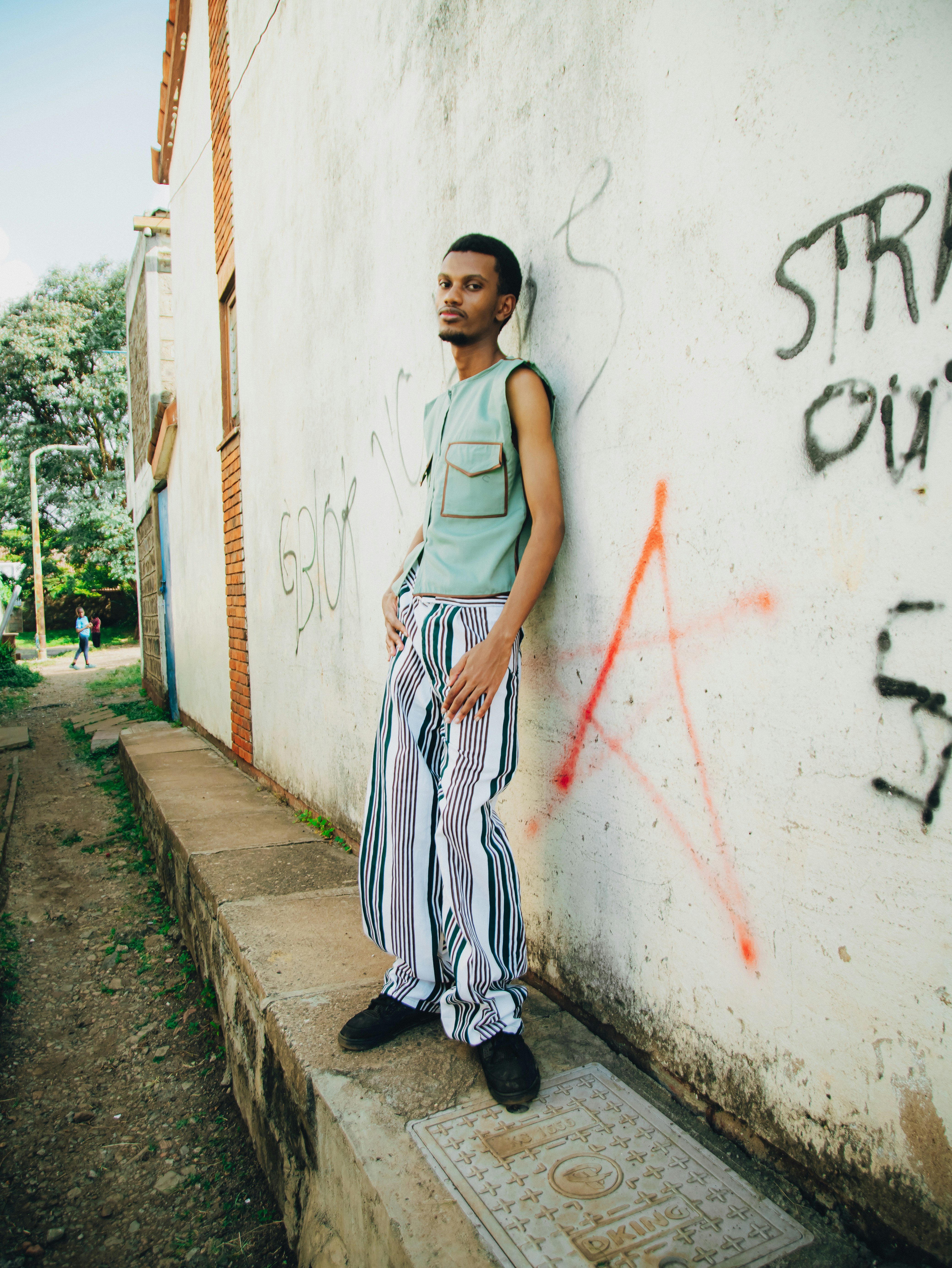 Young man in striped pants leaning against a graffiti wall.