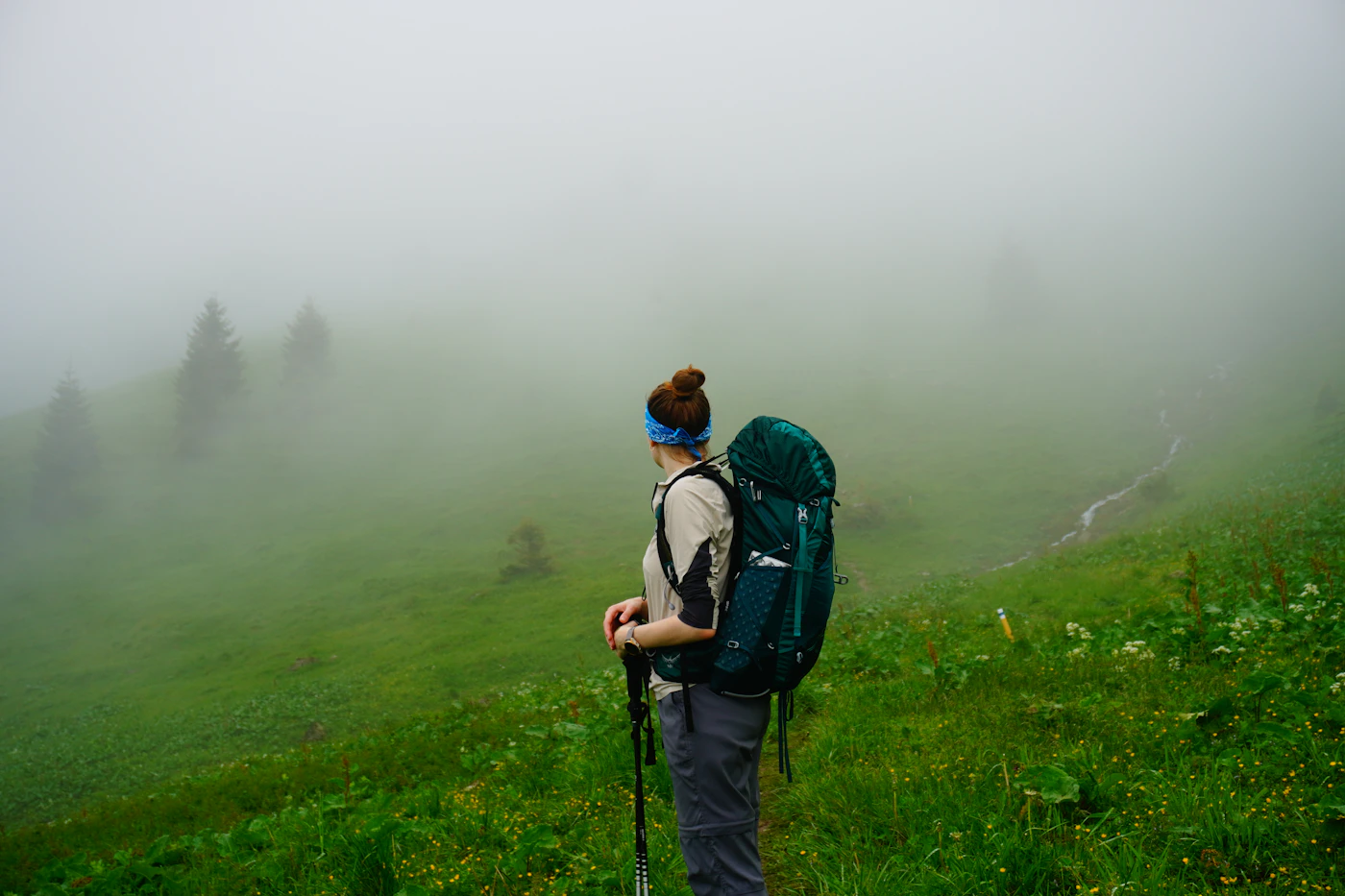 Senderista con mochila y bastones entre montañas verdes con niebla