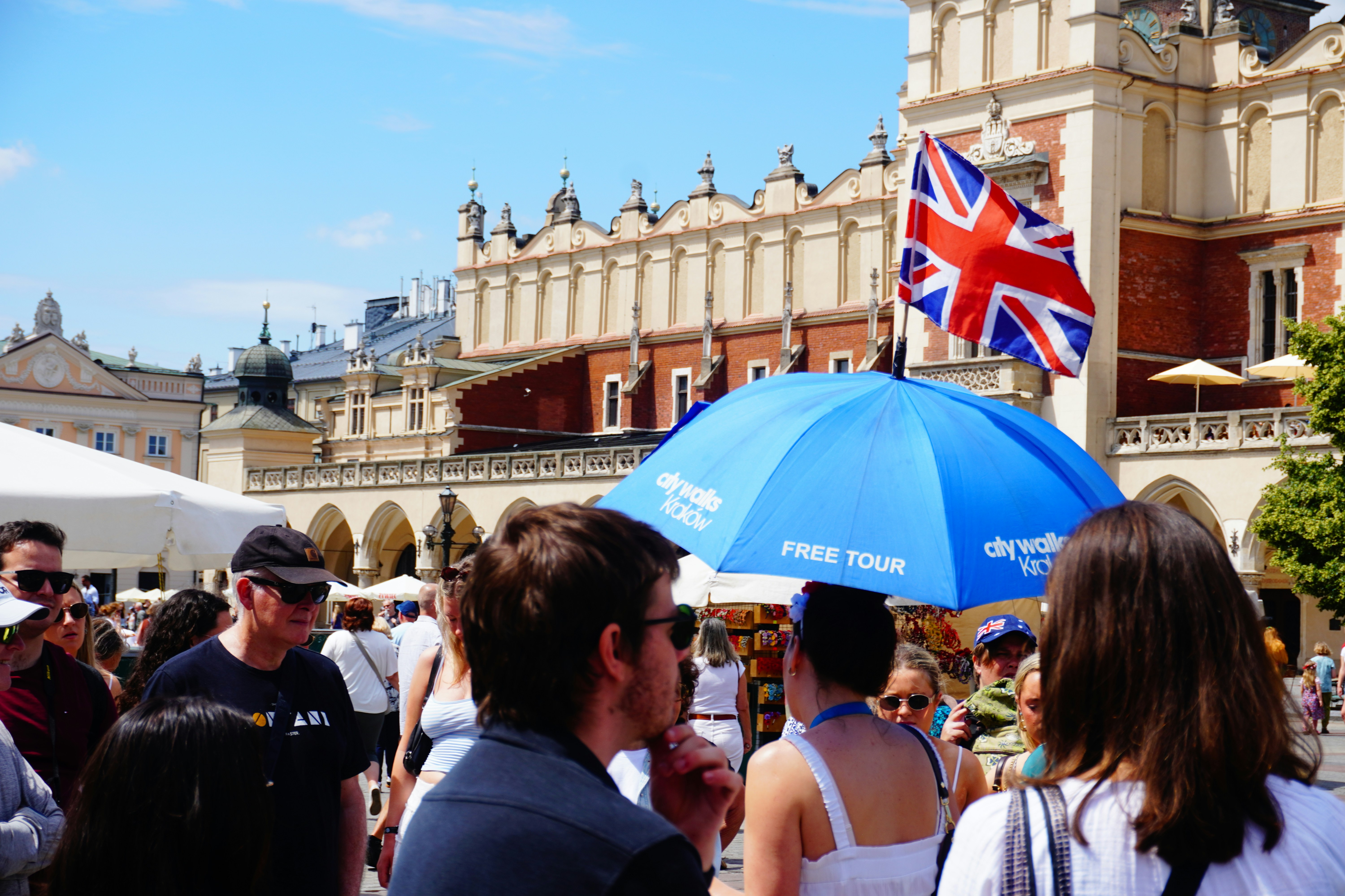 Crowded square with a blue umbrella and union jack flag.