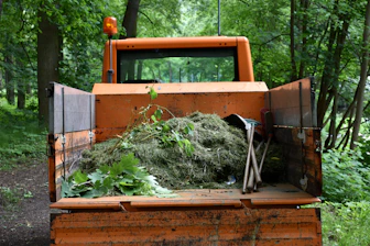 Orange utility truck carrying green garden waste in forest.