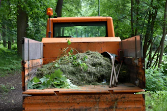 Orange utility truck carrying green garden waste in forest.