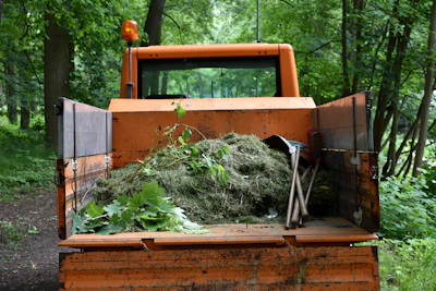 Orange utility truck carrying green garden waste in forest.