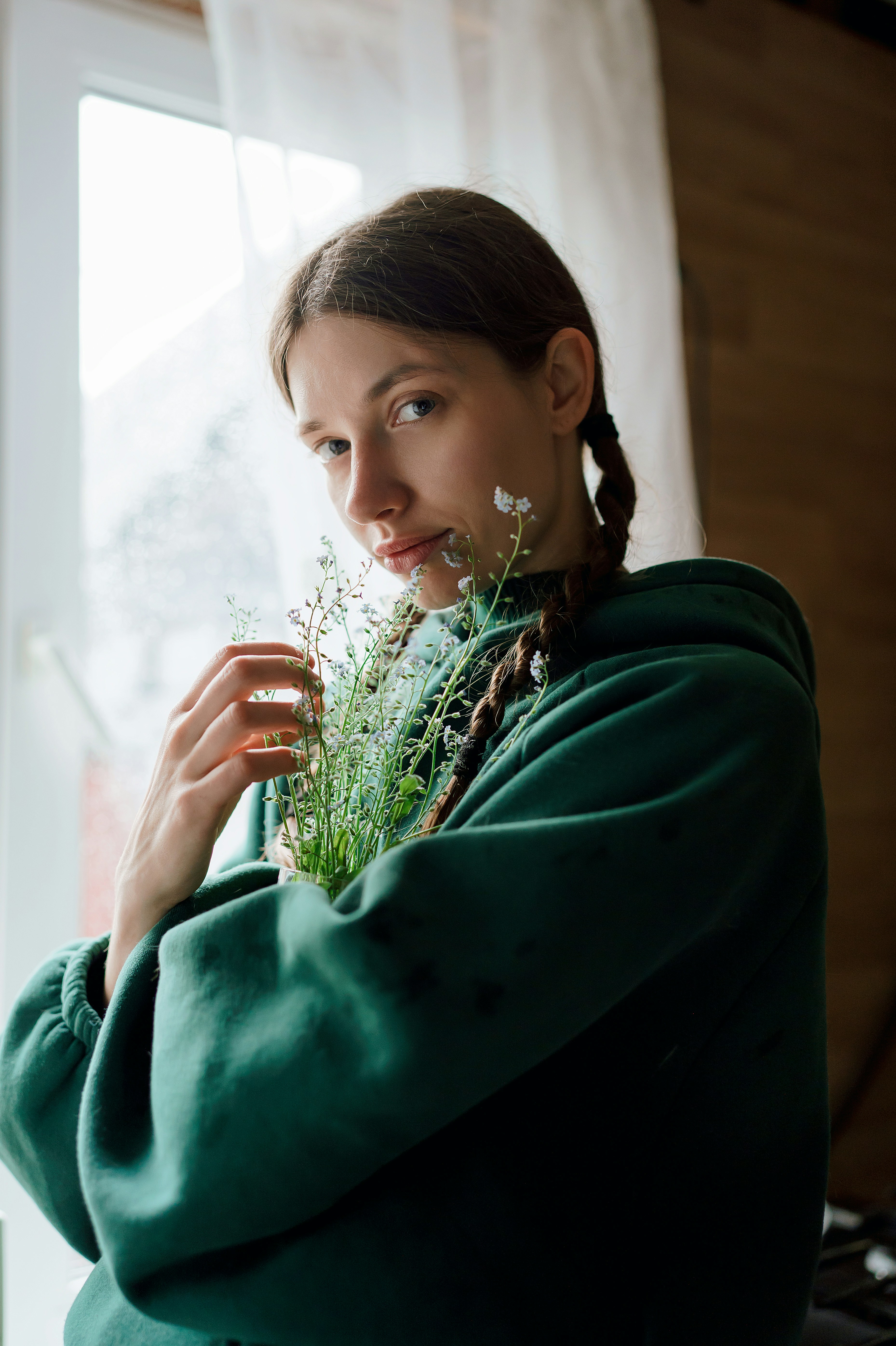 Young woman in green hoodie holding delicate white flowers.